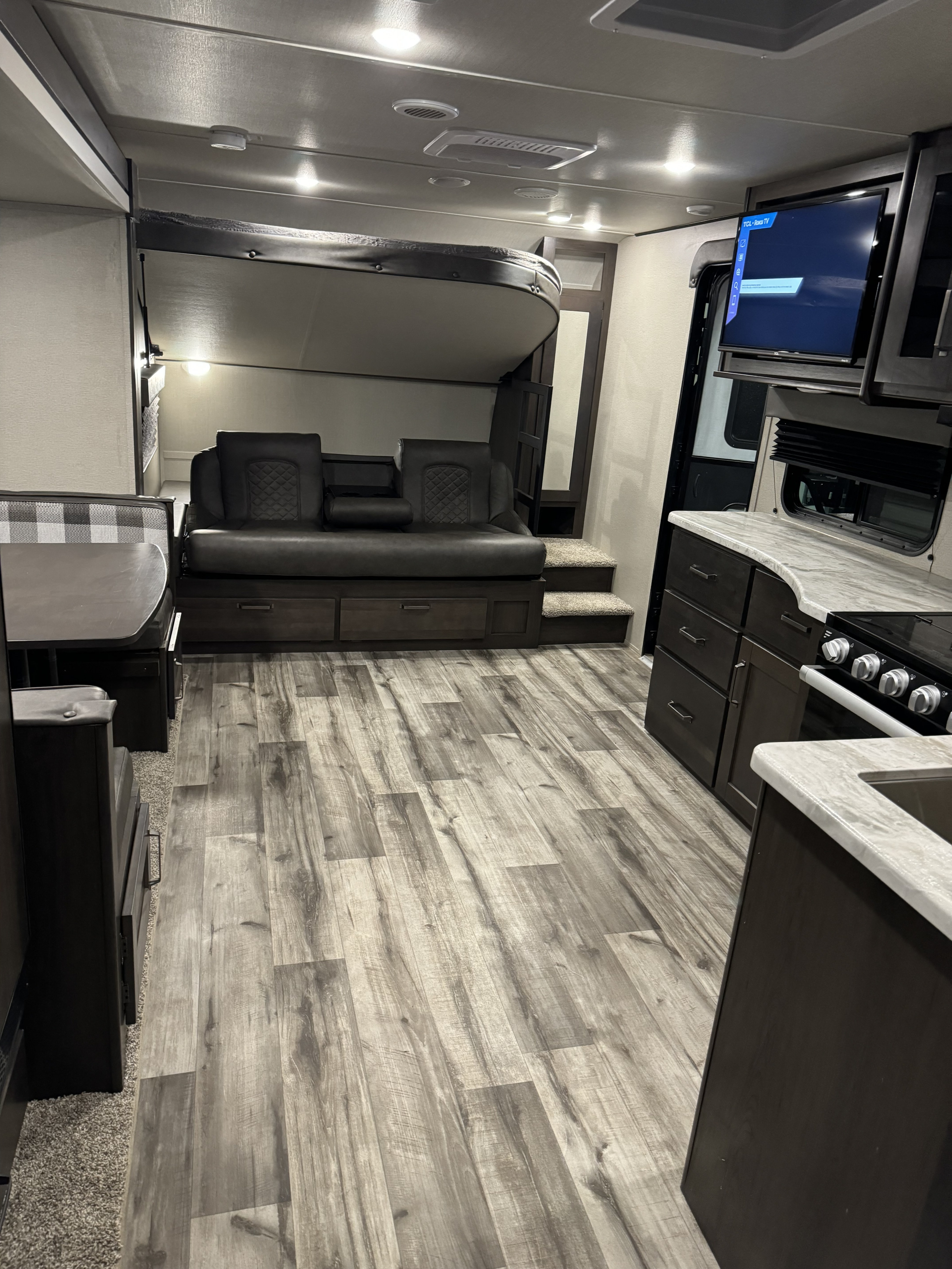 Modern RV rental living space with wood-look flooring, versatile sofa, drop-down bed, and full kitchen amenities.. Grand Design Transcend Xplor 2023