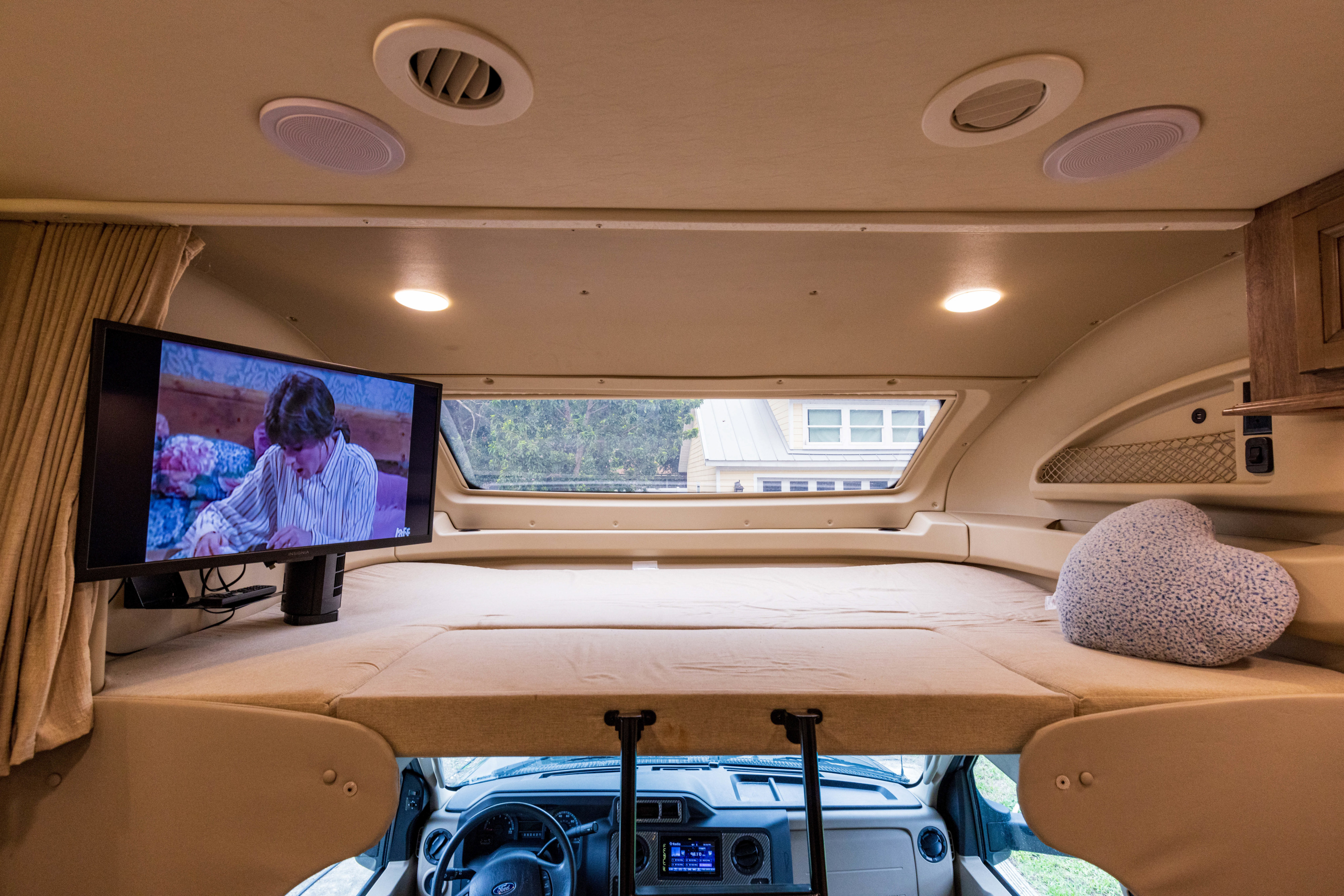 RV rental's cab-over bunk with mattress, TV, and window offers a cozy sleeping space.. Jayco Greyhawk Prestige 2020