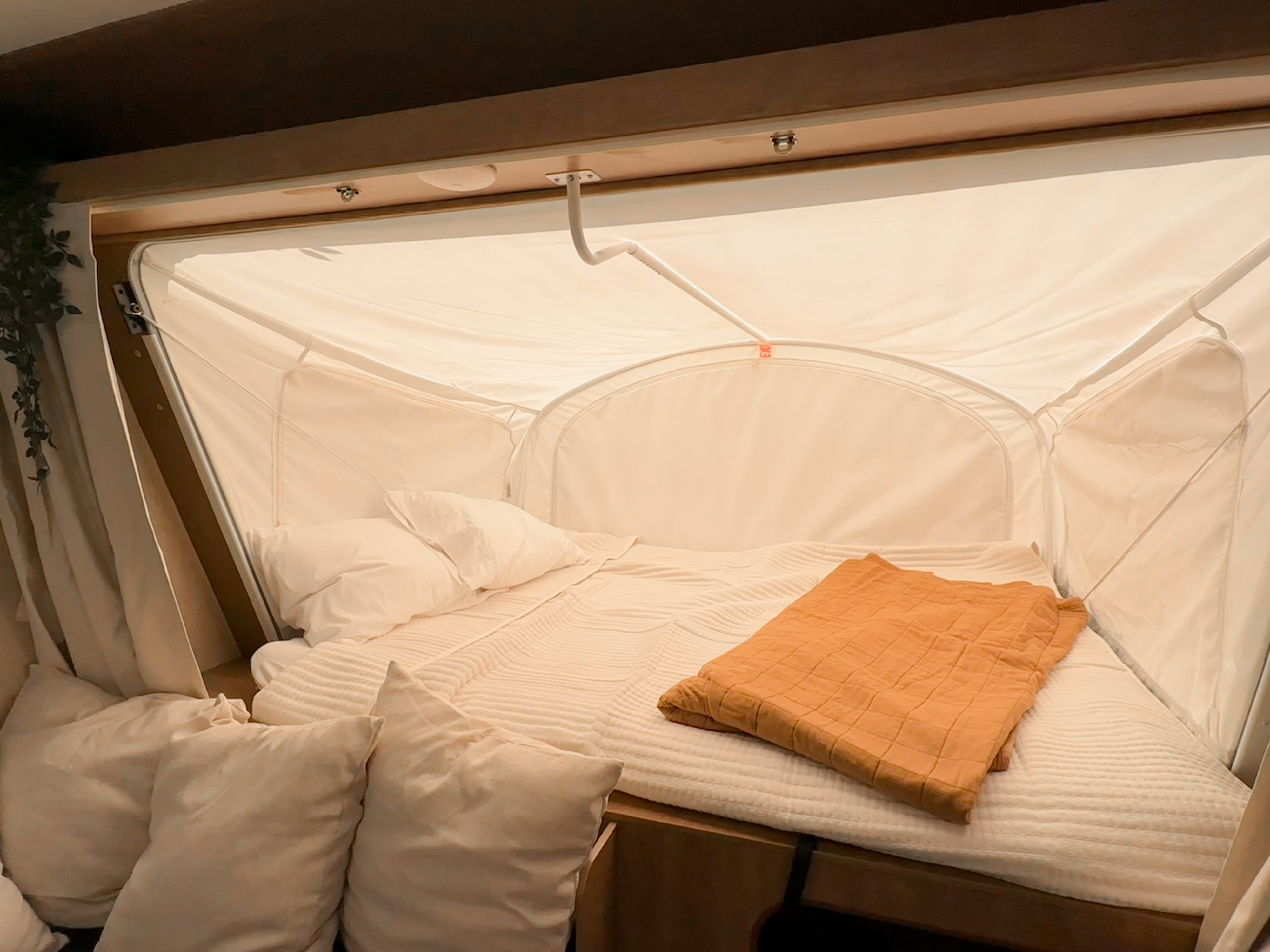Cozy RV rental bed with white linens, pillows, and an orange blanket inside a pop-up camper.. Starcraft Launch Mini 2018