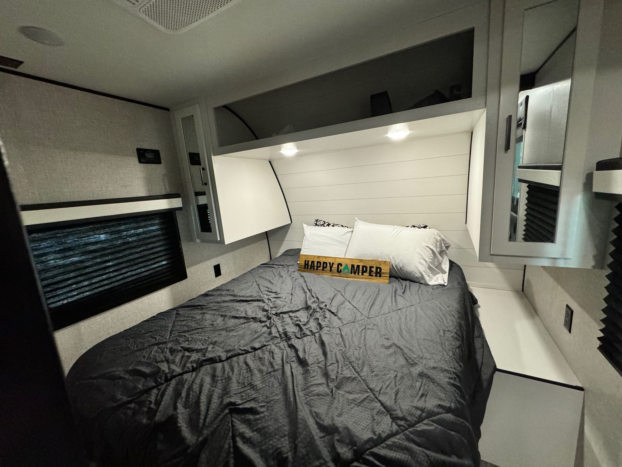 Cozy RV rental bedroom with a comfy bed, white pillows, and a 'HAPPY CAMPER' sign. Features modern shiplap walls & reading lights.. Jayco 284bhs 2024