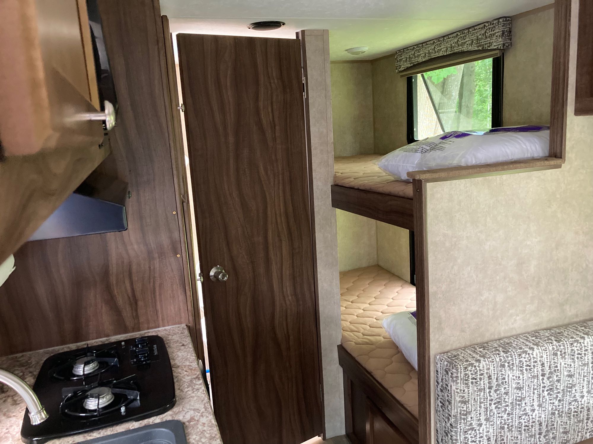RV rental interior featuring a compact kitchen with stove, a closed door, and cozy bunk beds with pillows.. Viking 17BH 2018