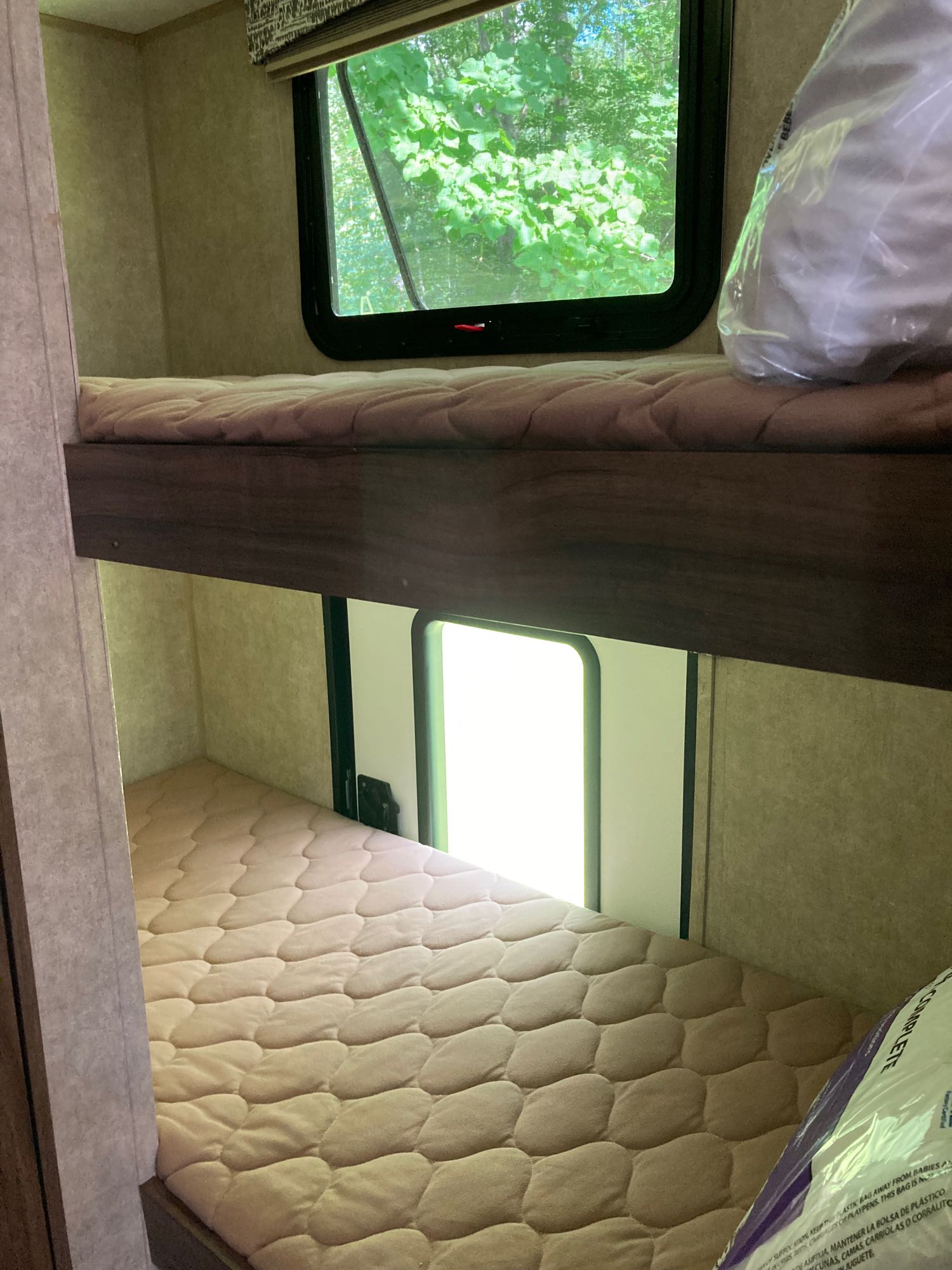 Cozy RV rental bunk beds with quilted mattresses. Windows offer views of outdoor greenery.. Viking 17BH 2018