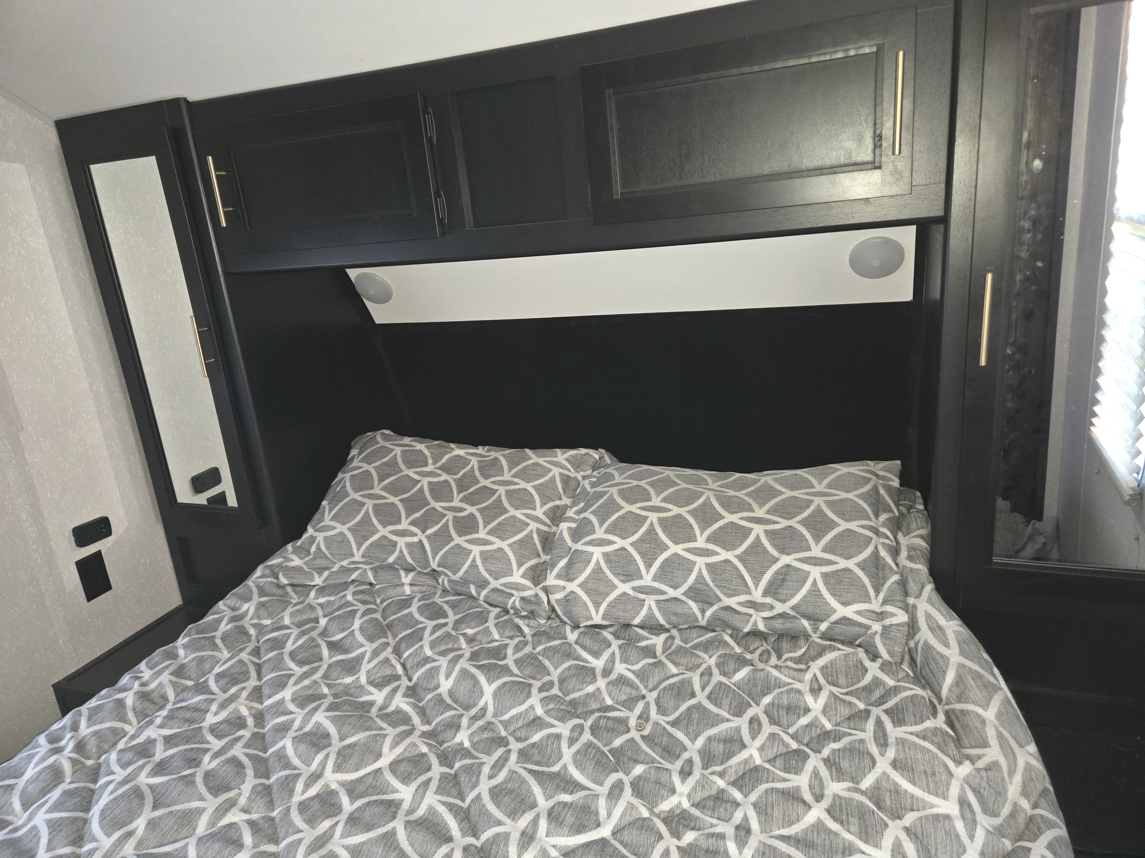 Cozy RV rental bedroom featuring gray patterned bedding, dark overhead cabinets, and integrated lighting.. Forest River Cherokee Grey Wolf 2021