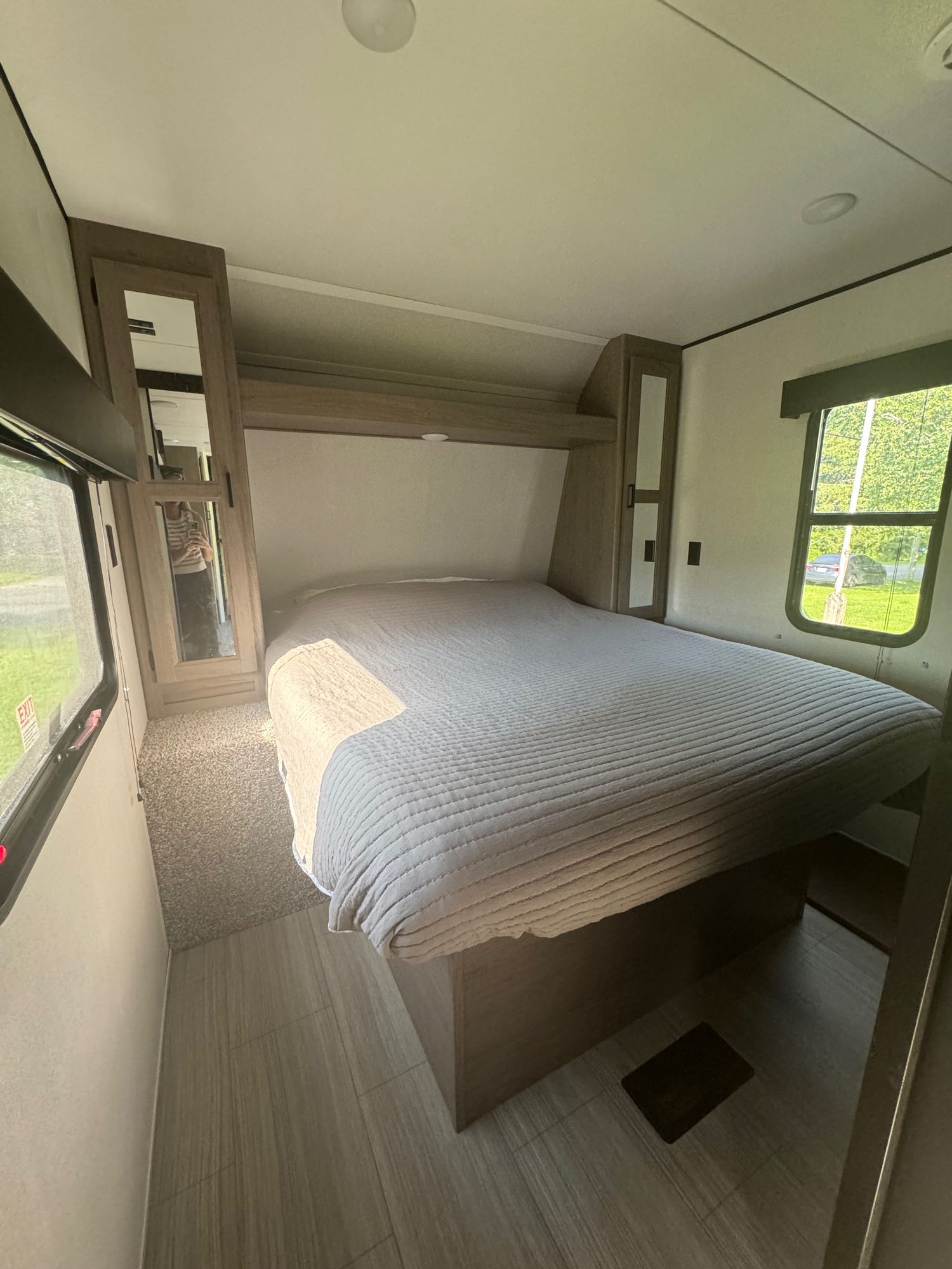 Cozy RV rental bedroom: bed with grey quilt, mirrored wardrobes, and windows showing green outdoor scenery.. Keystone RV Hideout 2021
