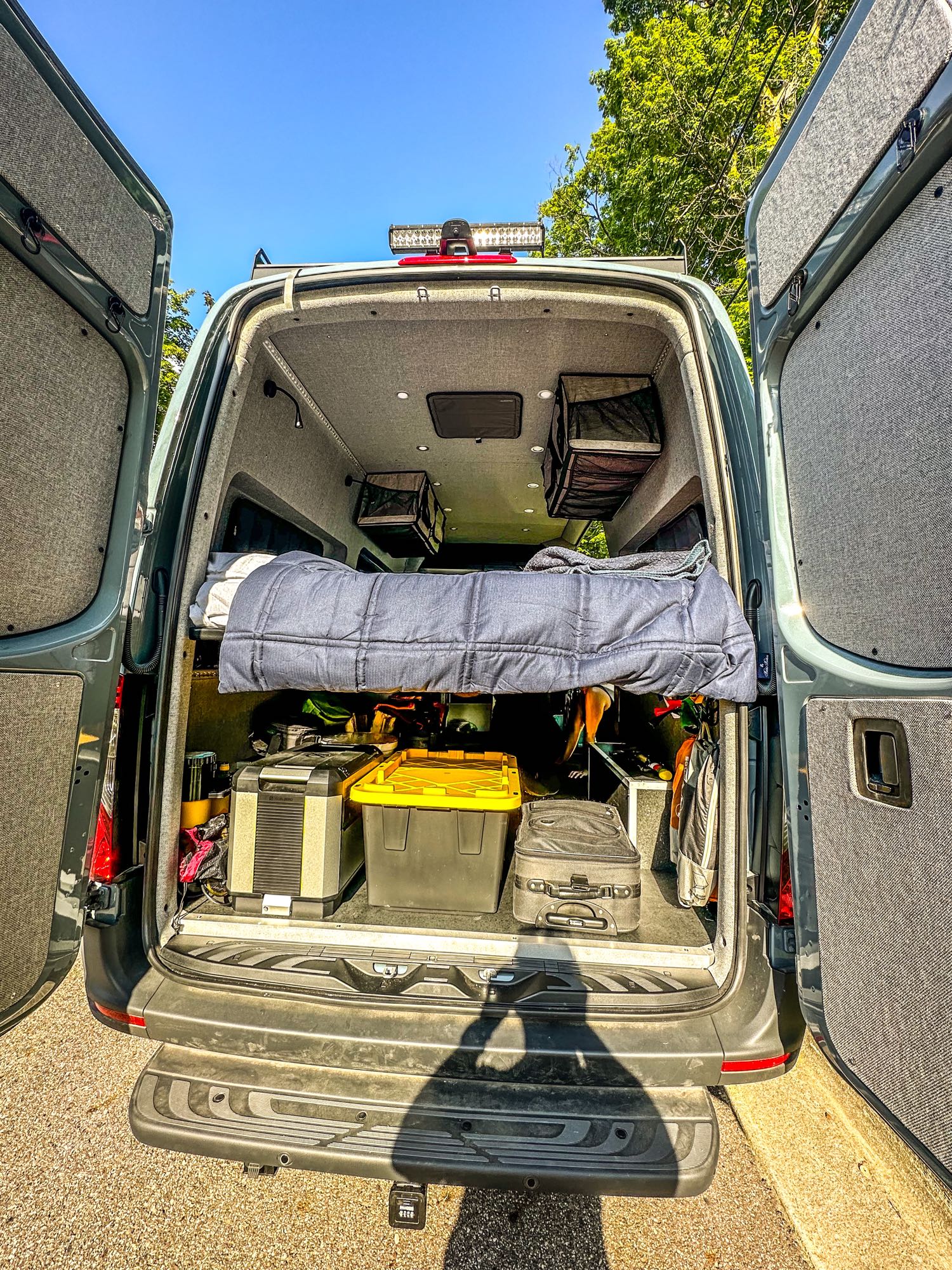 RV rental: Back of a cozy camper van showing a raised bed, under-bed storage, and custom interior for road trip adventures.. Mercedes-Benz Sprinter 2024