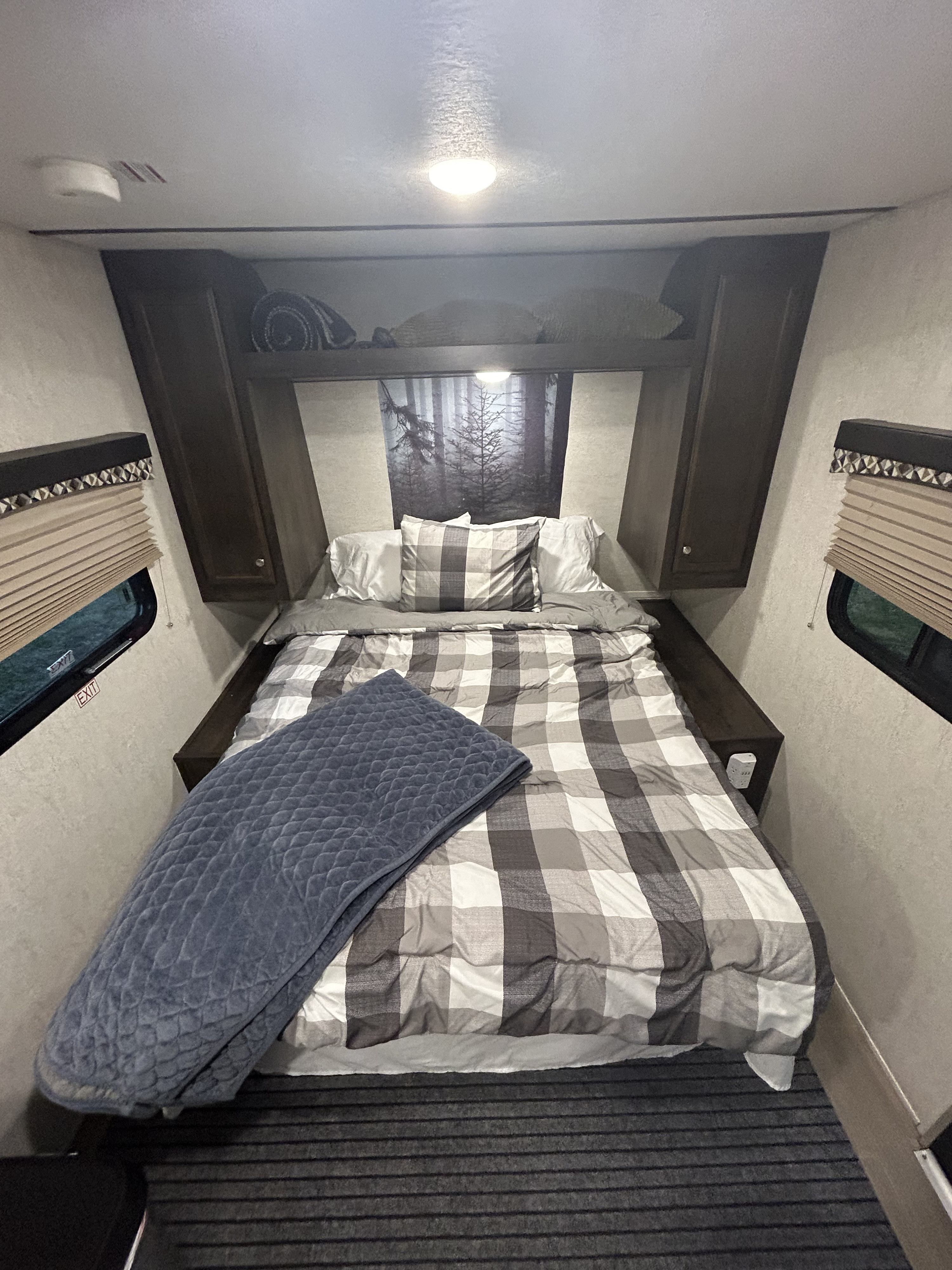 RV rental bedroom with plaid bedding, cozy blue blanket, overhead cabinets, and forest wall art for comfy travels.. Starcraft Launch Outfitter 2018