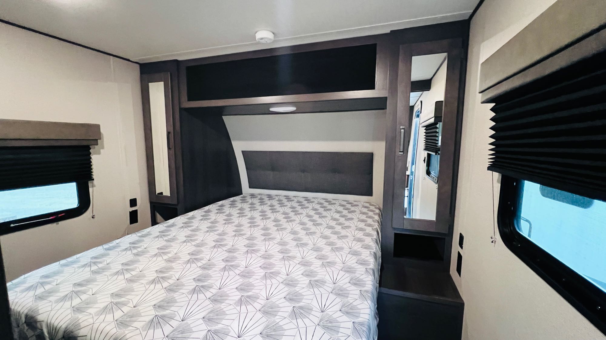 RV rental bedroom with a comfortable bed, built-in storage, and windows with blinds. Enjoy cozy travel trailer lodging.. Grand Design Transcend Xplor 2022
