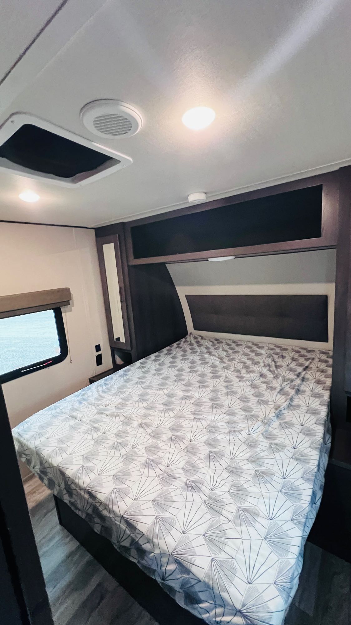 RV rental bedroom featuring a geometric patterned bed, overhead storage, and a window. Bright, compact, and ready for travel.. Grand Design Transcend Xplor 2022