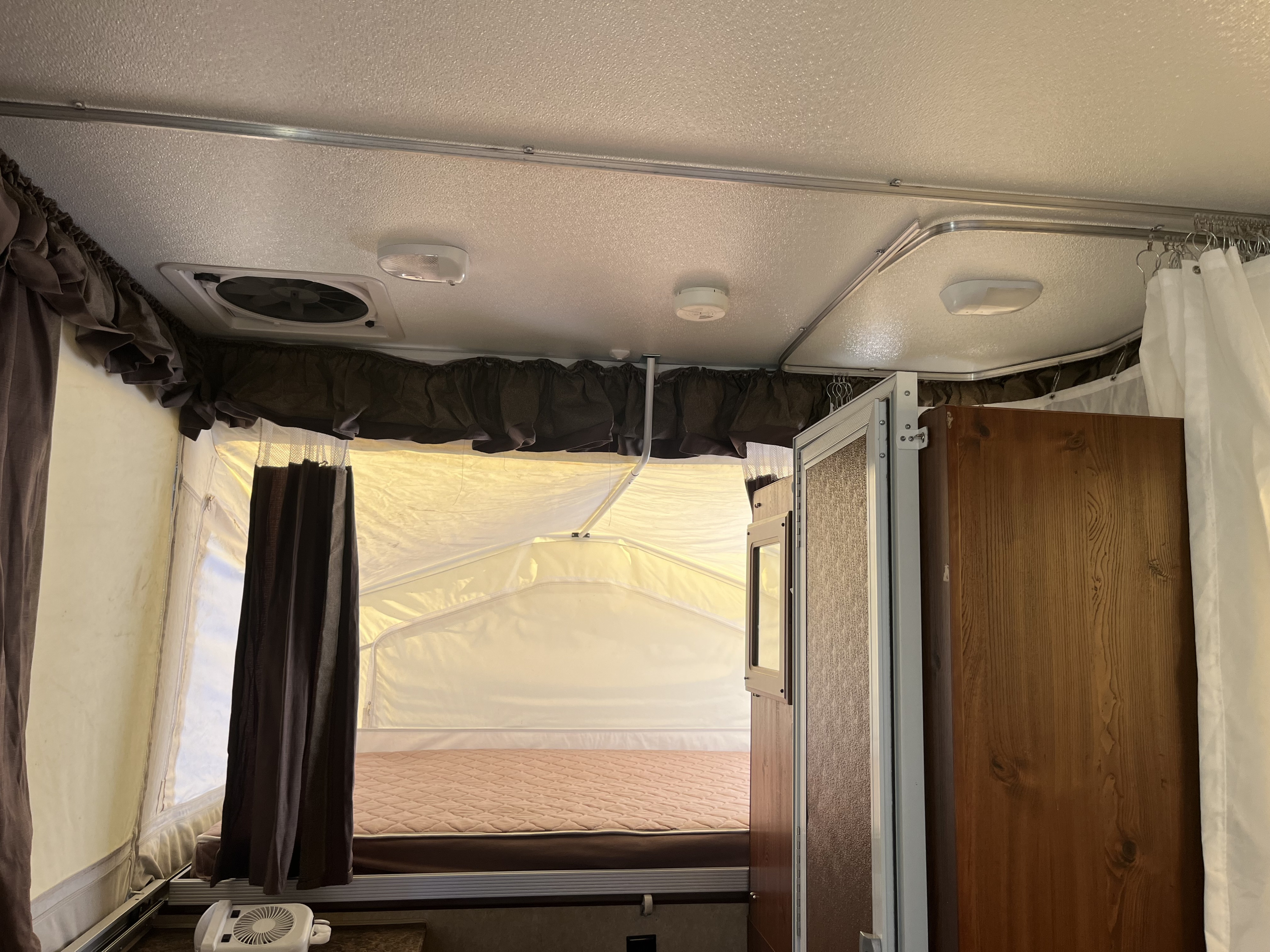 Inside an RV rental pop-up camper: a quilted bed, ceiling fan, and brown curtains create a snug sleeping area.. Forest River Rockwood Roo 2011