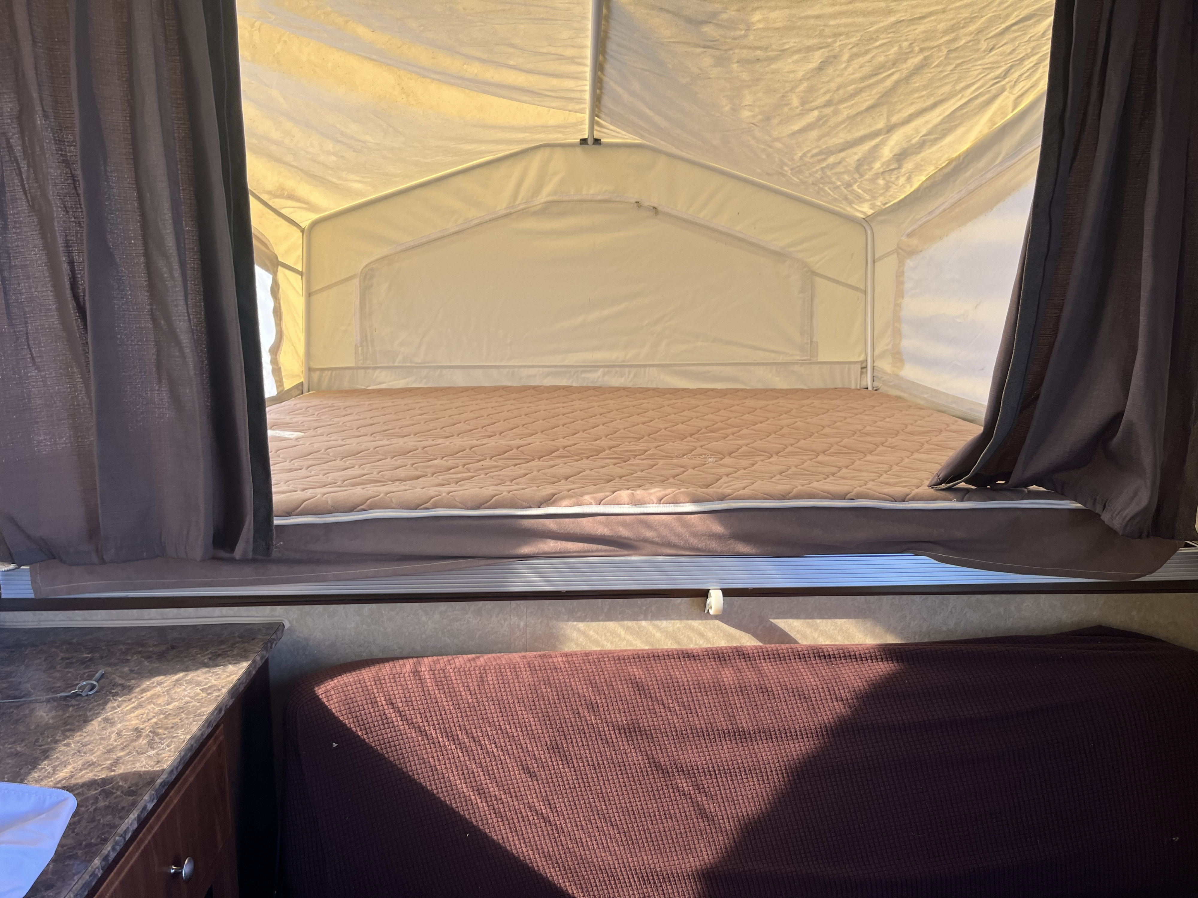 Cozy pop-up RV rental interior. Features a large bed with quilted brown mattress, curtains, and bright canvas walls.. Forest River Rockwood Roo 2011