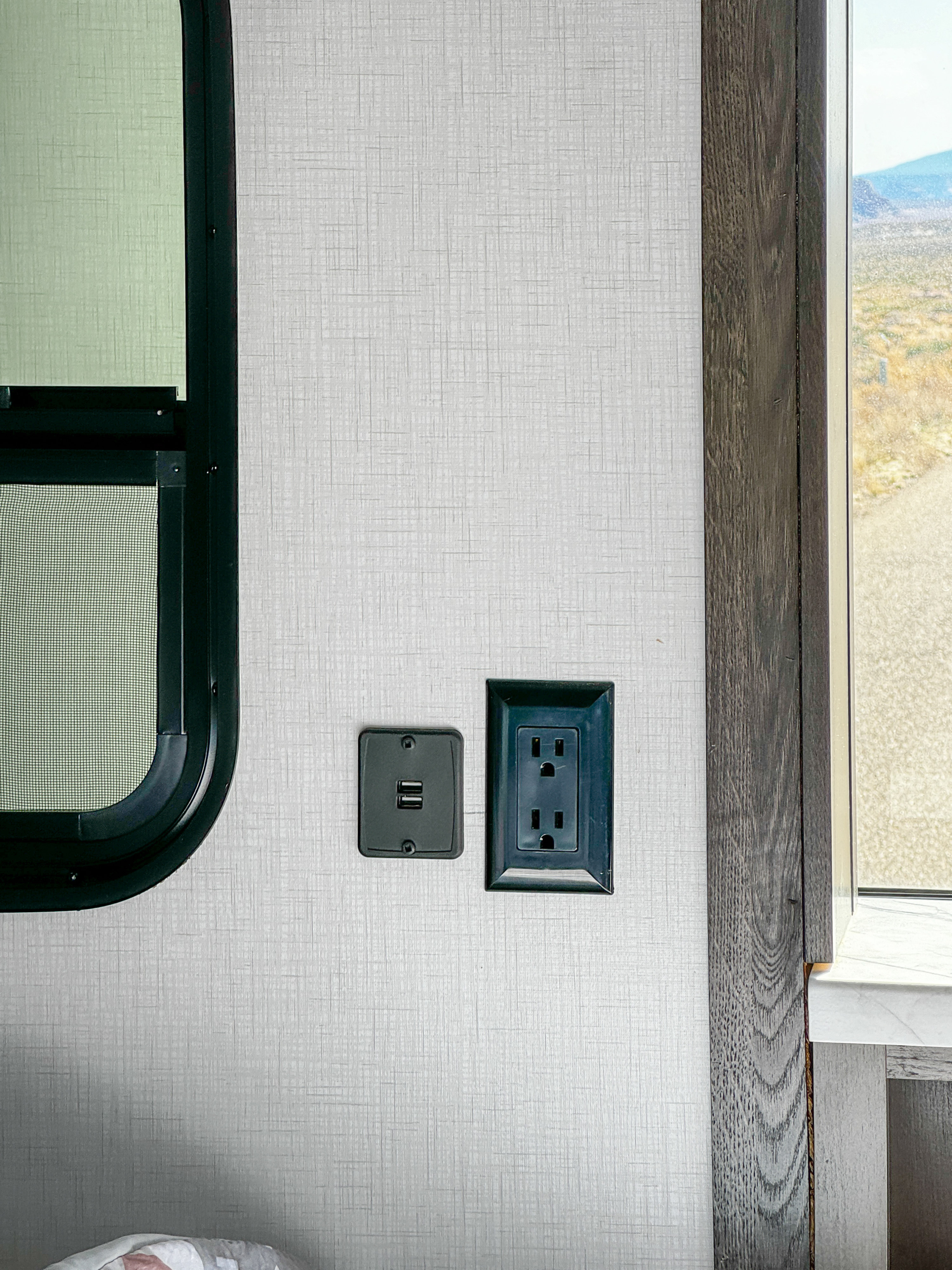 RV rental interior: USB & AC outlets on a textured wall next to a dark-framed window overlooking a scenic landscape.. FR3 FR3 Motorhome 2023