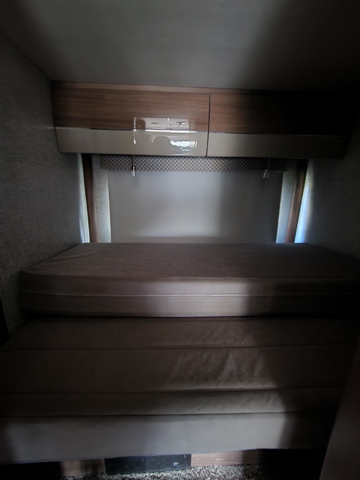 RV rental bunk beds with overhead storage, showing a comfortable, dimly lit sleeping area perfect for a cozy camper interior.. Winnebago Navion 24G 2017