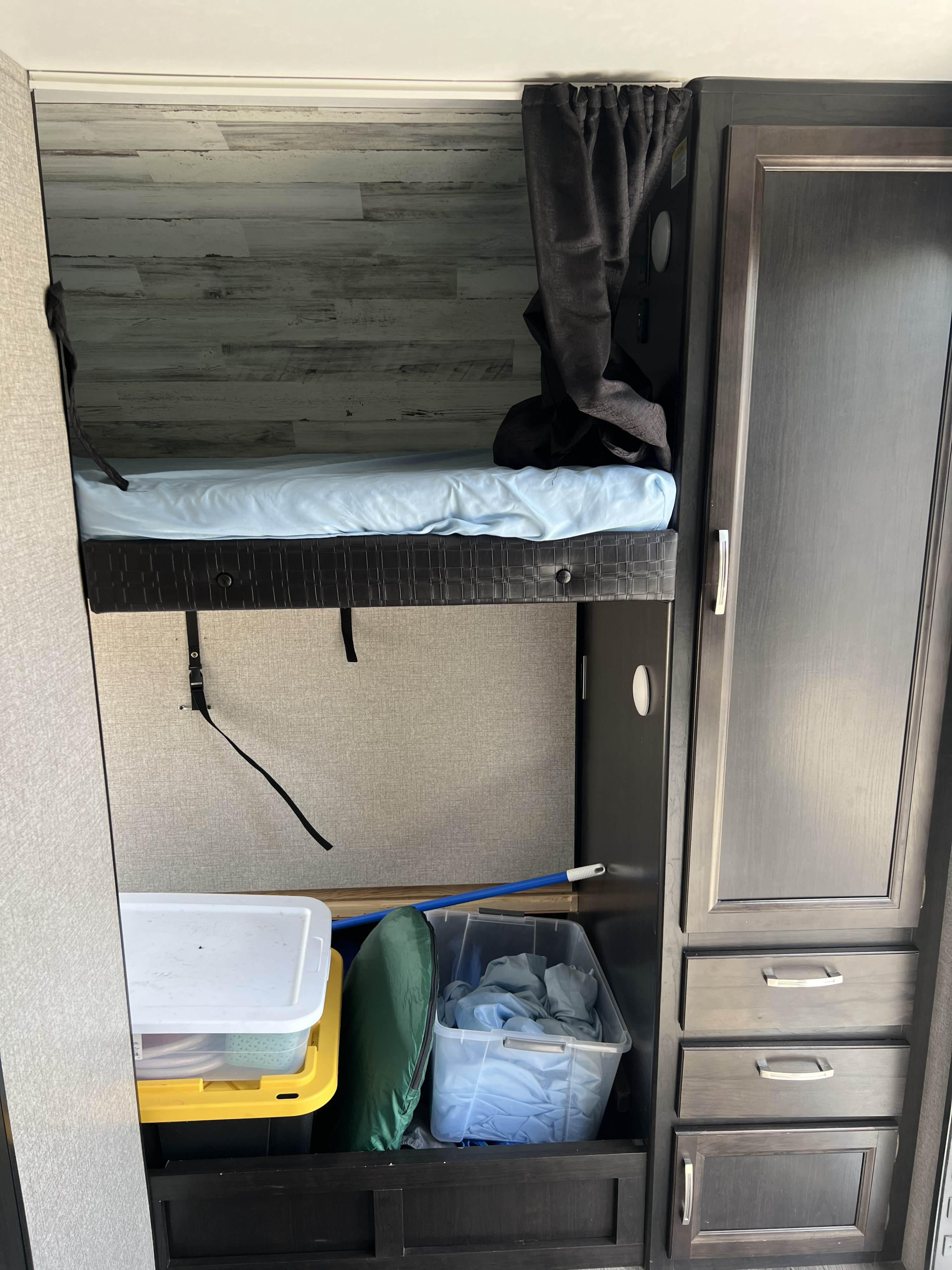 Inside an RV rental: a compact bunk bed with a light blue sheet, storage bins below, and dark wood cabinetry.. Jayco Jay Feather 2021