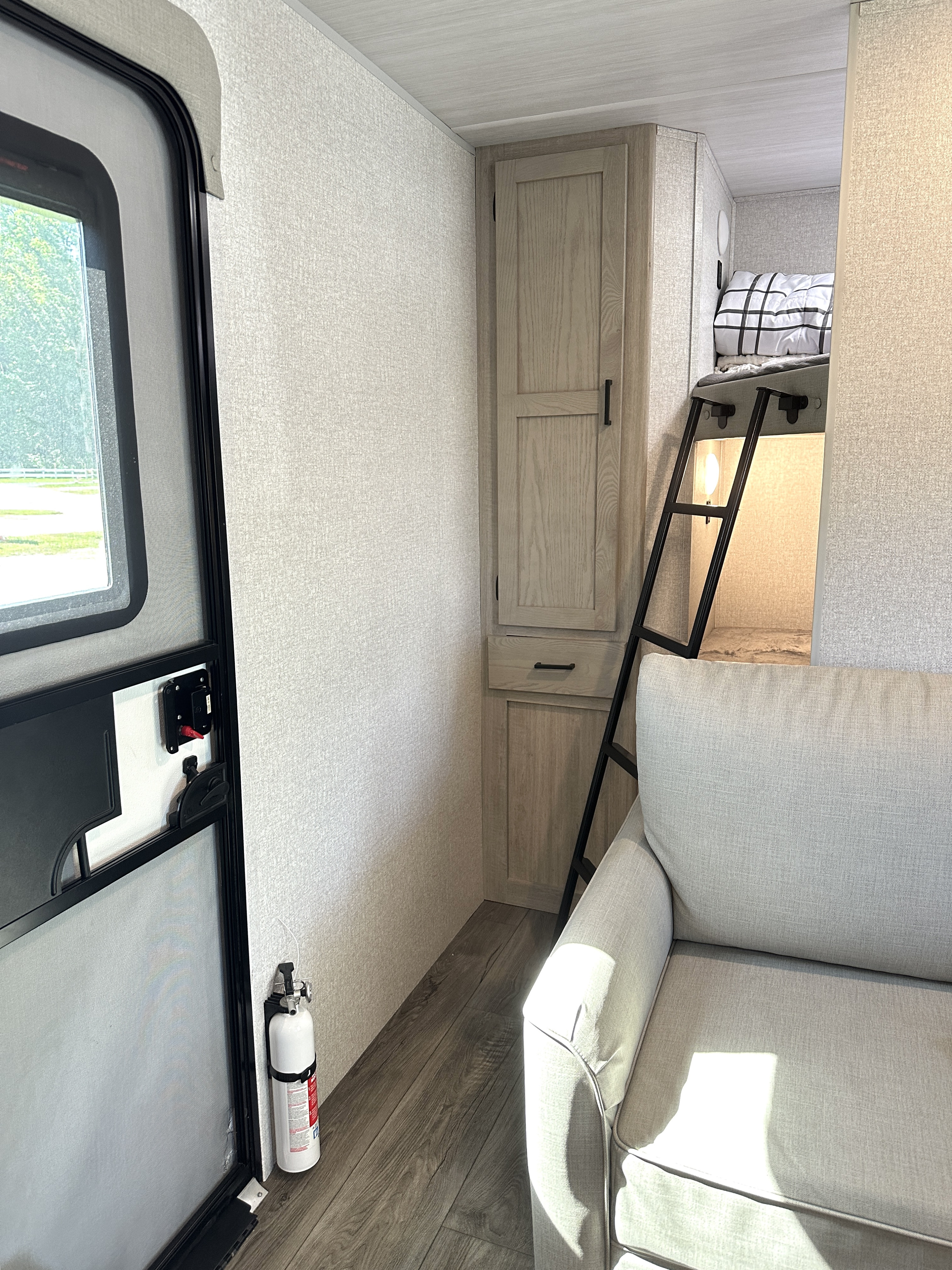 This RV rental's light-filled interior shows bunk beds with a ladder, a sofa, and a door. Note the mounted fire extinguisher.. East to West Alta 2022