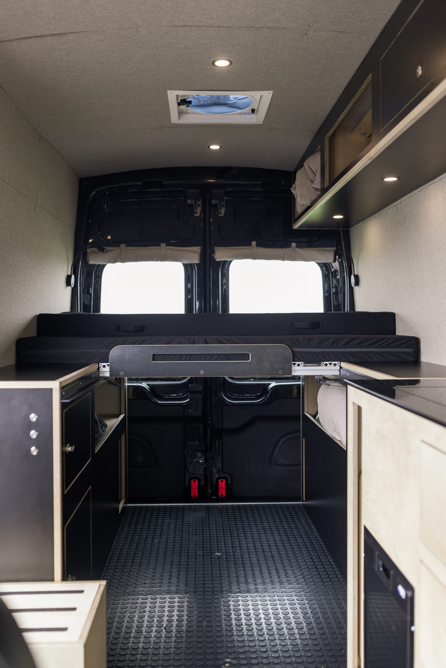 Interior of an rv rental camper van. Features a bed, storage units, pull-out table, & skylight.. Ford Transit 2020