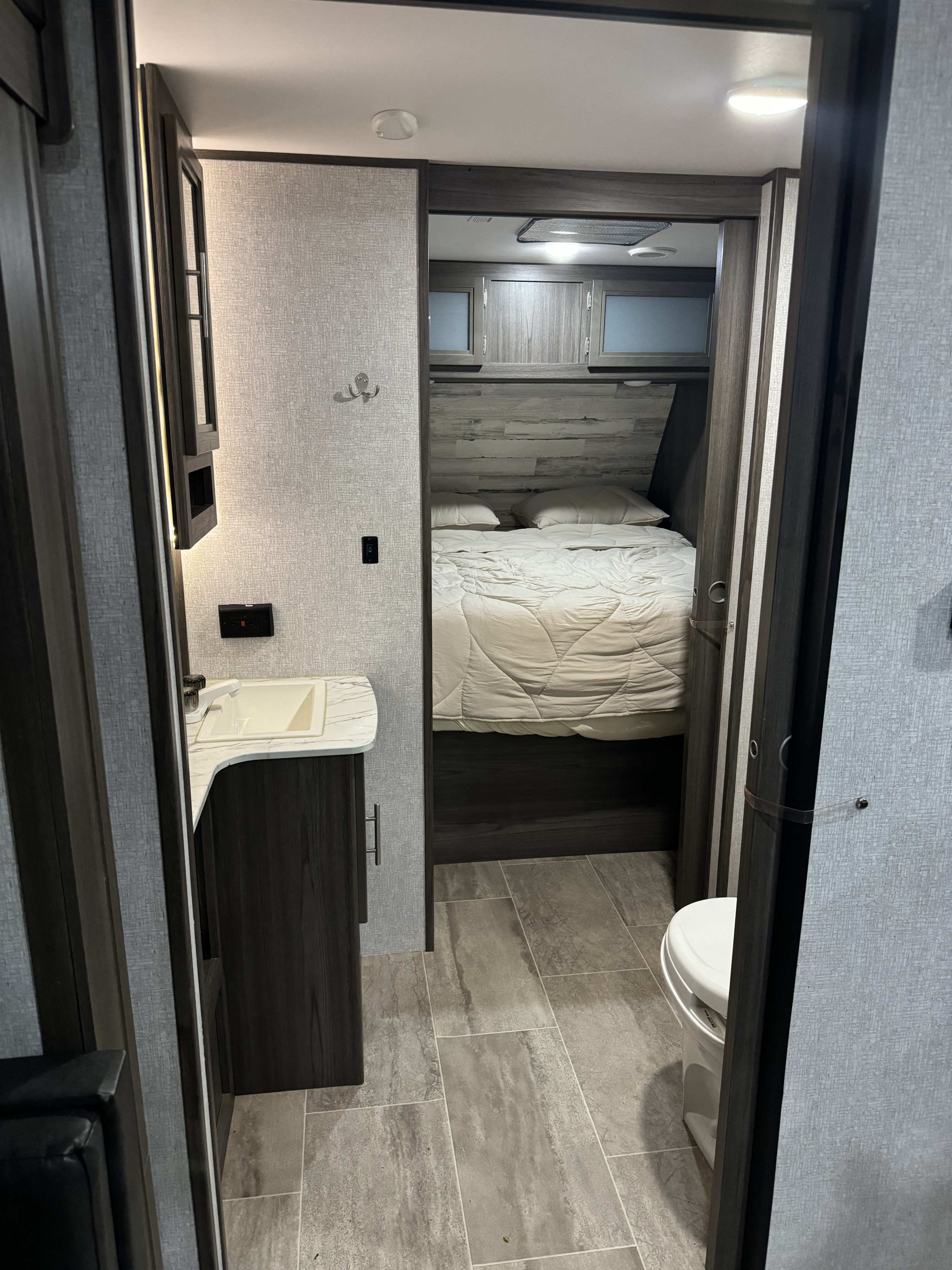 The bathroom and bedroom of a modern RV rental. Features vanity, sink, toilet, and bed.. Dutchmen Kodiak Ultra Lite 2020