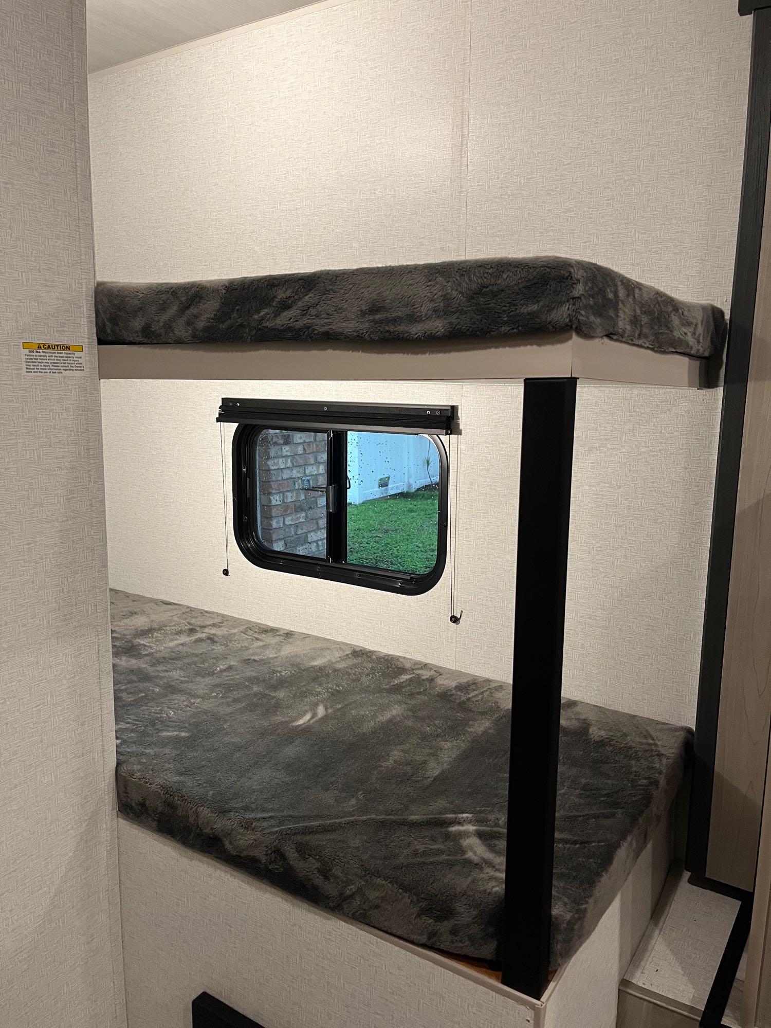 Cozy bunk beds inside an RV rental, featuring soft grey bedding and a window in the lower bunk with an outdoor view.. Keystone RV Springdale 2024