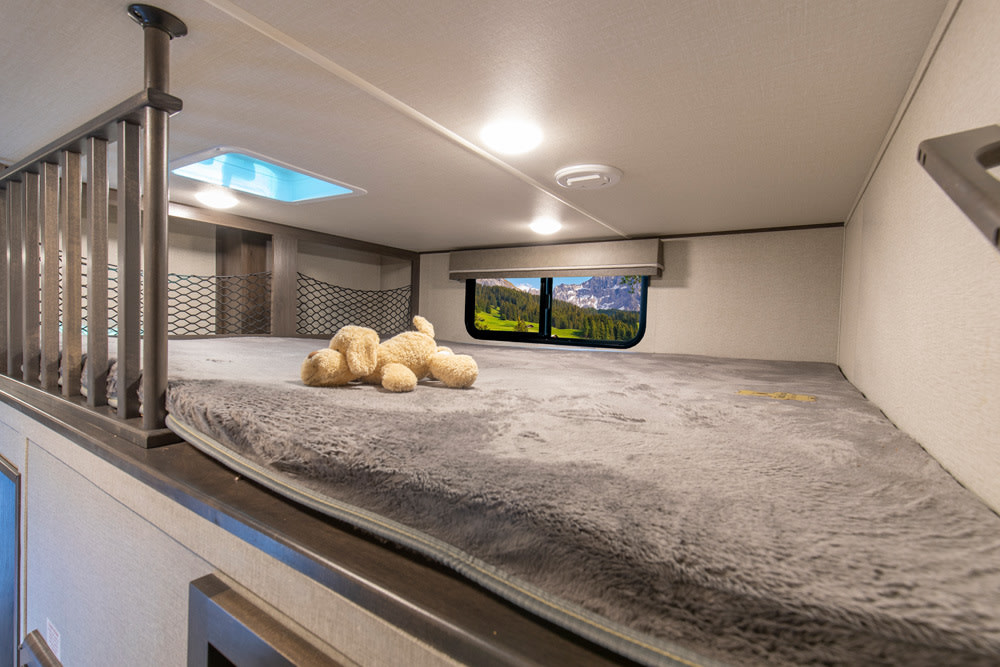Cozy RV rental bunk bed with a plush mattress, stuffed dog, and mountain view window, ideal for travel.. Grand Design Reflection 2023