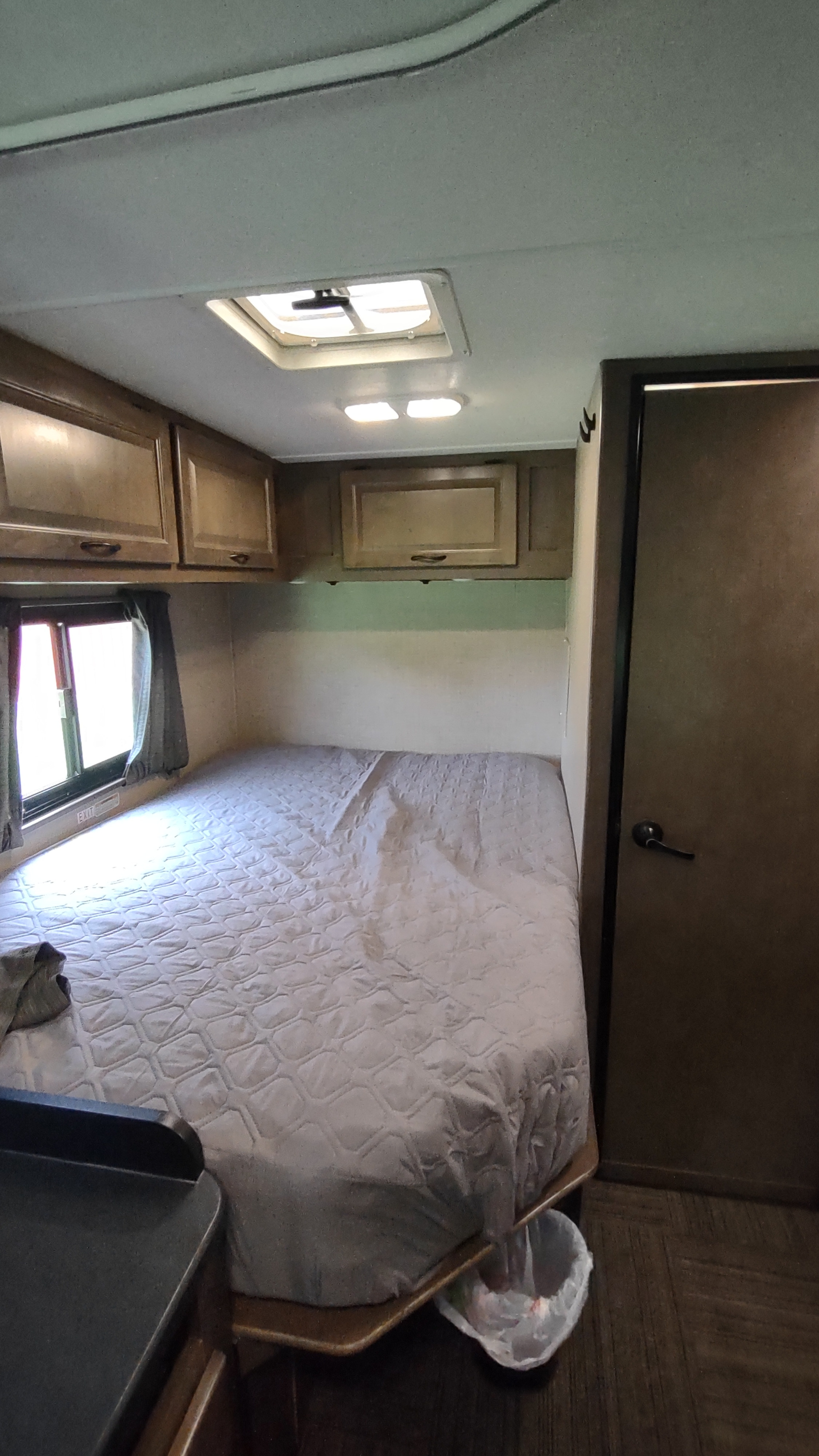 Step inside this RV rental's compact bedroom featuring a cozy bed, overhead storage cabinets, and natural light from the window.. Thor Motor Coach Four Winds Majestic 2019