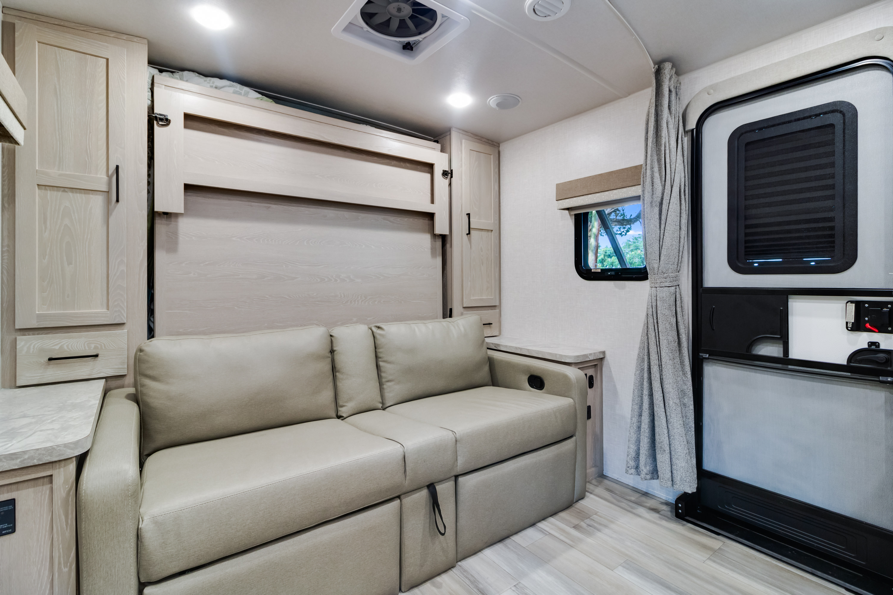 Experience comfort in this modern rv rental interior, featuring a cozy sofa, fold-down Murphy bed, and light wood finishes.. Forest River Flagstaff Micro Lite 2022
