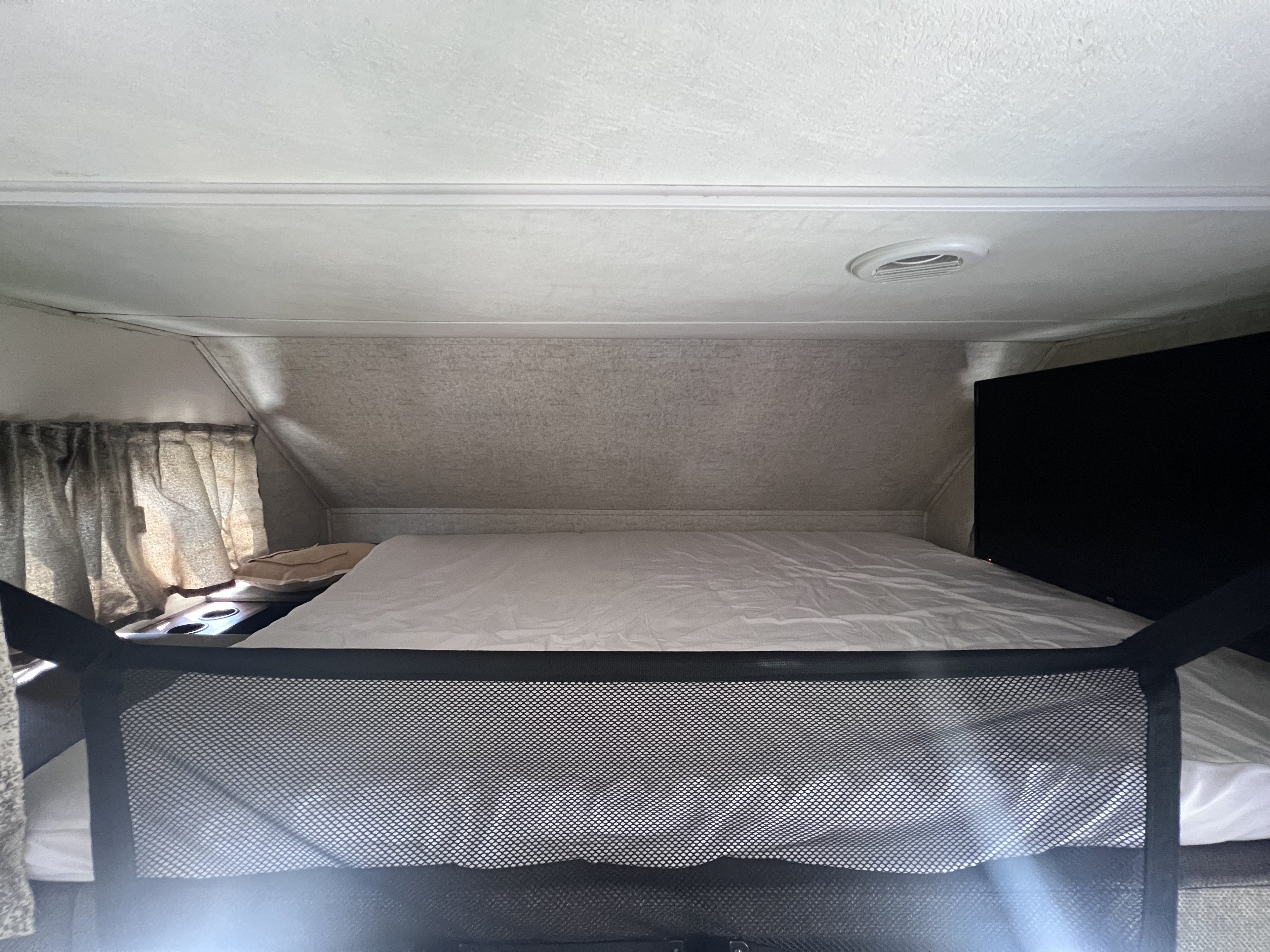 Cozy overhead sleeping area in an RV rental, featuring a bed, safety net, side curtains, and a TV for comfort.. Forest River Forester 2019