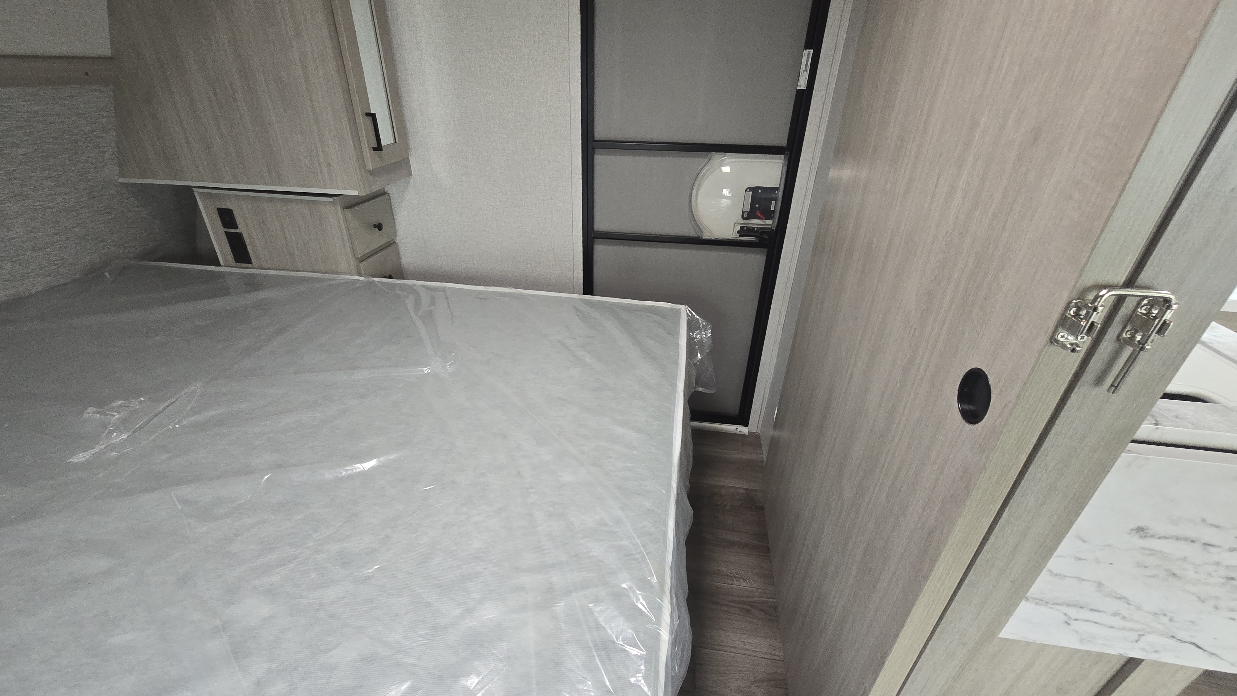 RV rental bedroom: New mattress in plastic, light wood cabinets, and modern door visible.. East to West Alta 2022