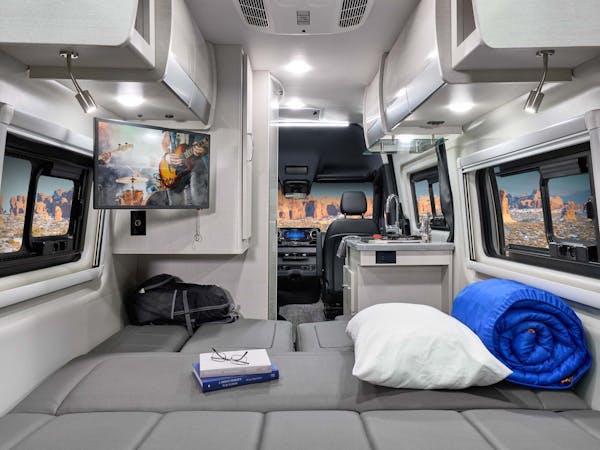 Inside a cozy rv rental: modern camper van interior with convertible bed, kitchen, TV, and scenic desert window views.. Thor Motor Coach Sanctuary 2023