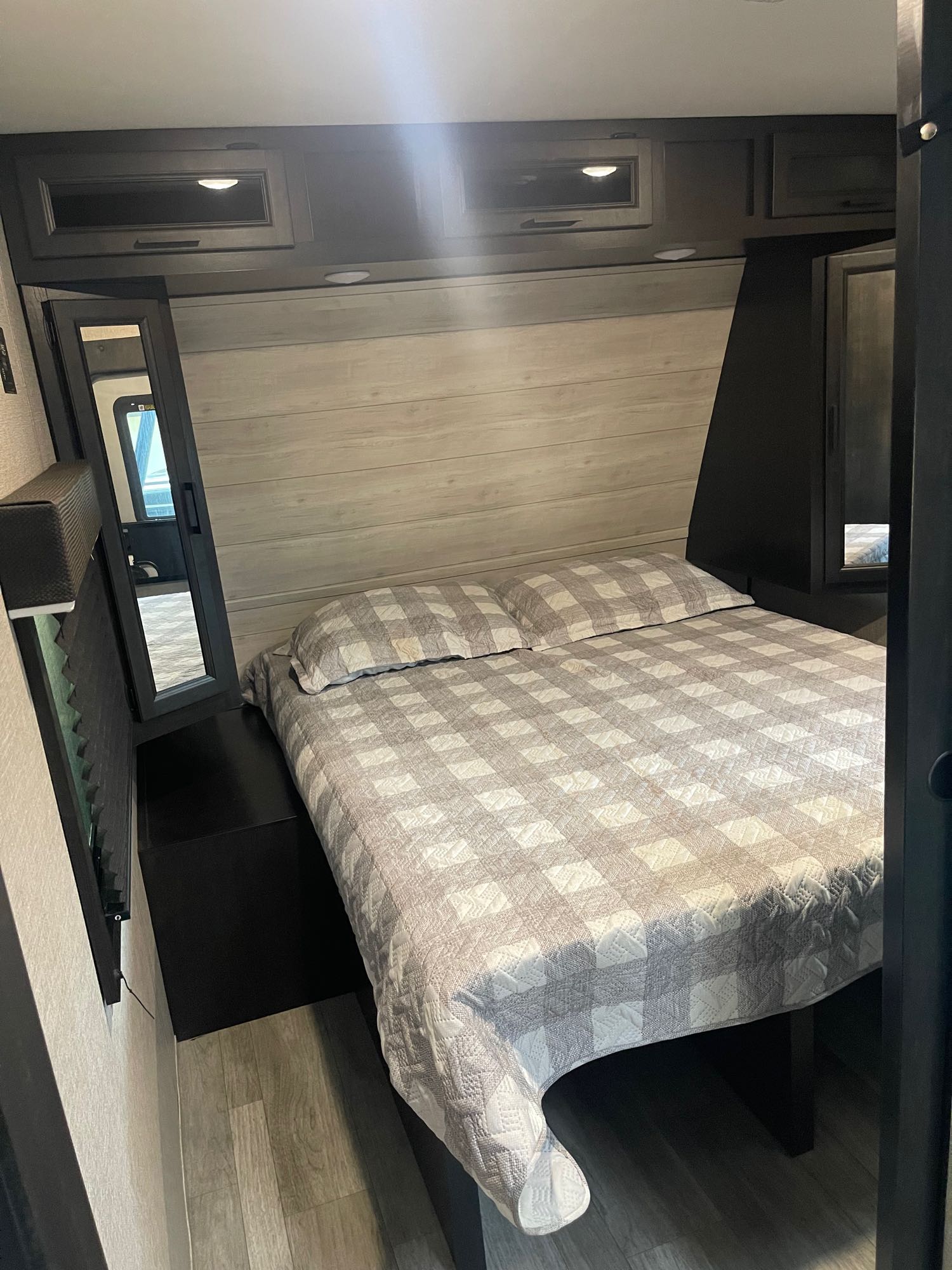 Cozy RV rental bedroom featuring a comfy, checkered bed, overhead cabinets, and light wood-paneled walls for a relaxing stay.. Jayco Jay Flight 2022