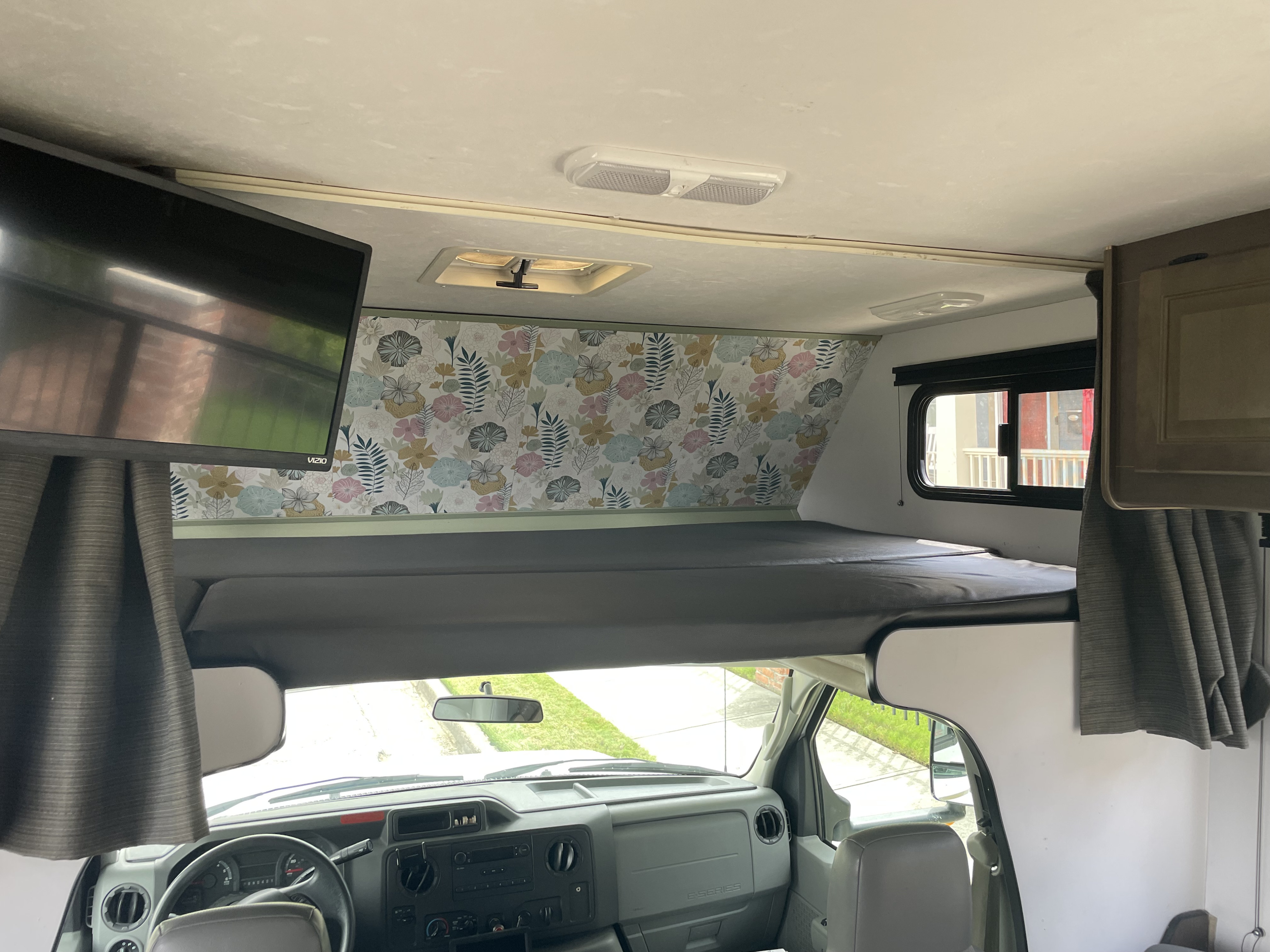 A bright and cozy RV rental interior, showcasing the overhead bunk, floral wallpaper, TV, and front cabin.. Thor Majestic 2019