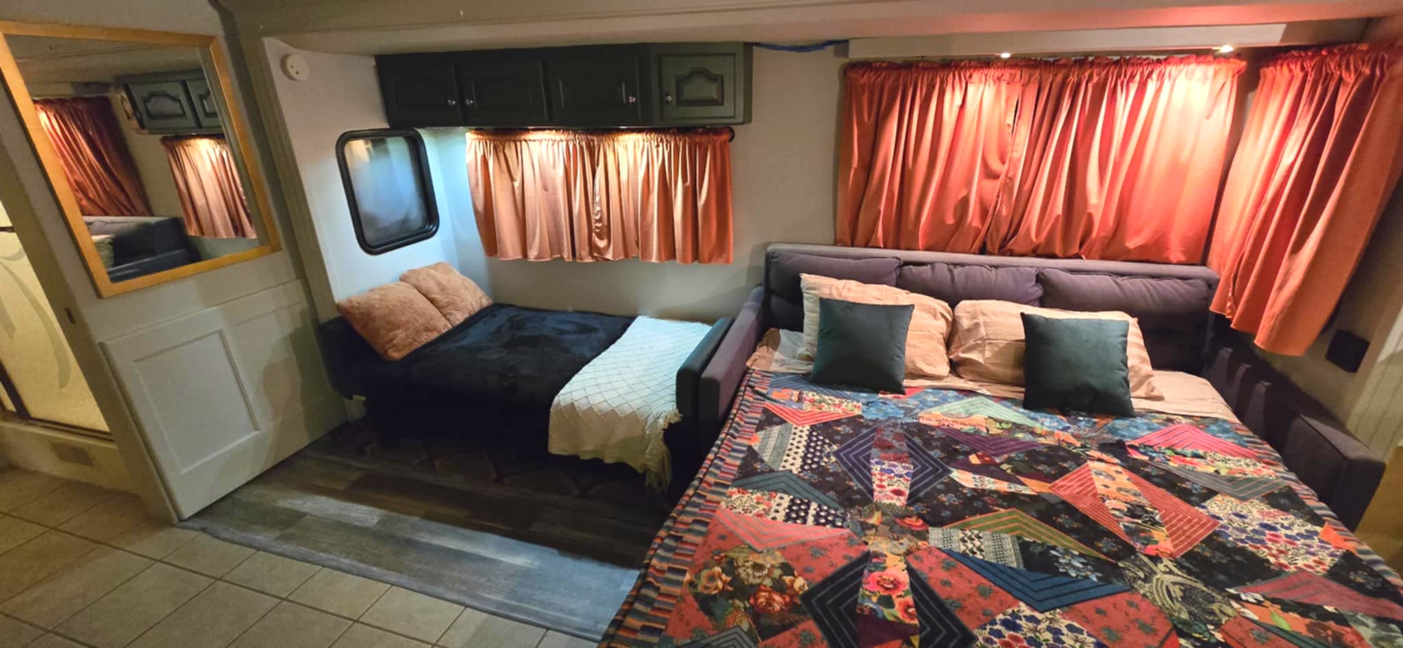 RV rental interior: A cozy space with two sofa beds, one covered by a vibrant patchwork quilt, and warm curtains.. Country Coach Allure 2004
