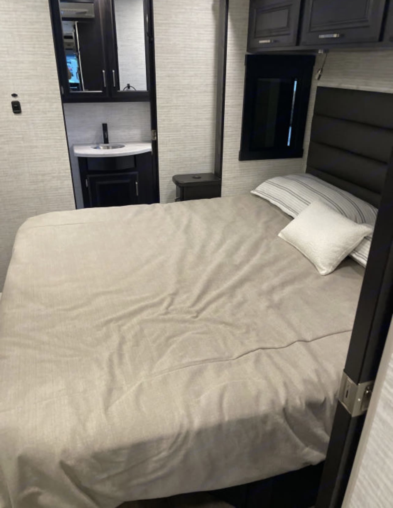 Cozy RV rental bedroom features a comfortable bed with light bedding, a compact vanity with sink, and dark cabinetry.. Entegra Coach Other 2024
