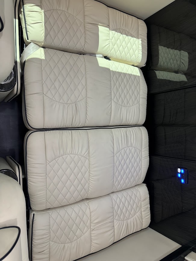 Cream quilted sleeping area in an RV rental. Four stacked cushions with dark piping line the interior wall.. Midwest Automotive Designs Ultimate Presidential 2020