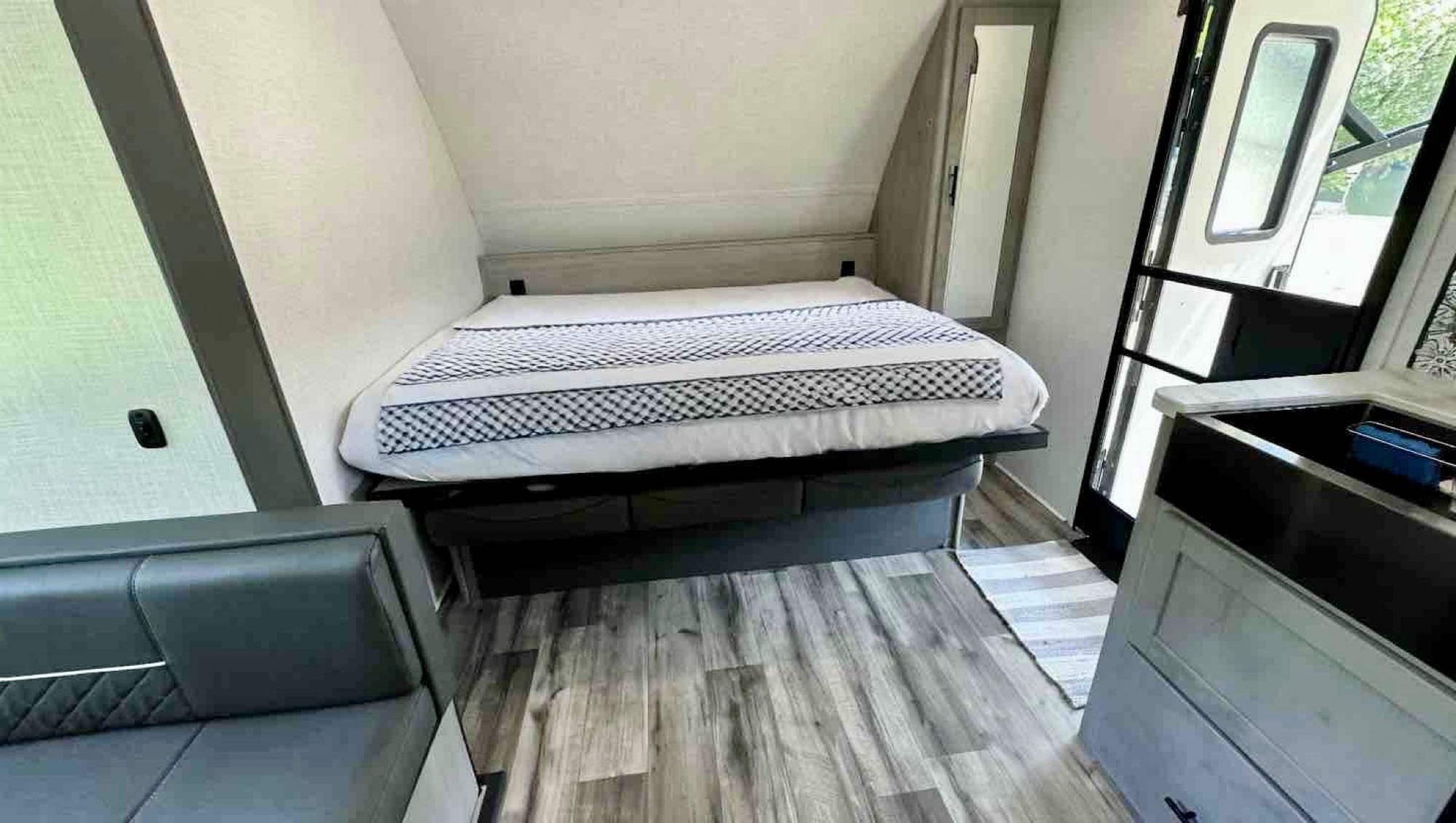 RV rental interior with comfortable bed, sleek couch, and kitchen sink. Wood-look flooring completes this cozy space.. Dutchmen Coleman Light 2023