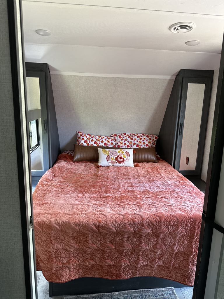 Spacious RV rental bedroom featuring a large bed with a vibrant coral quilt and built-in storage cabinets.. Aspen Trail LE 2022