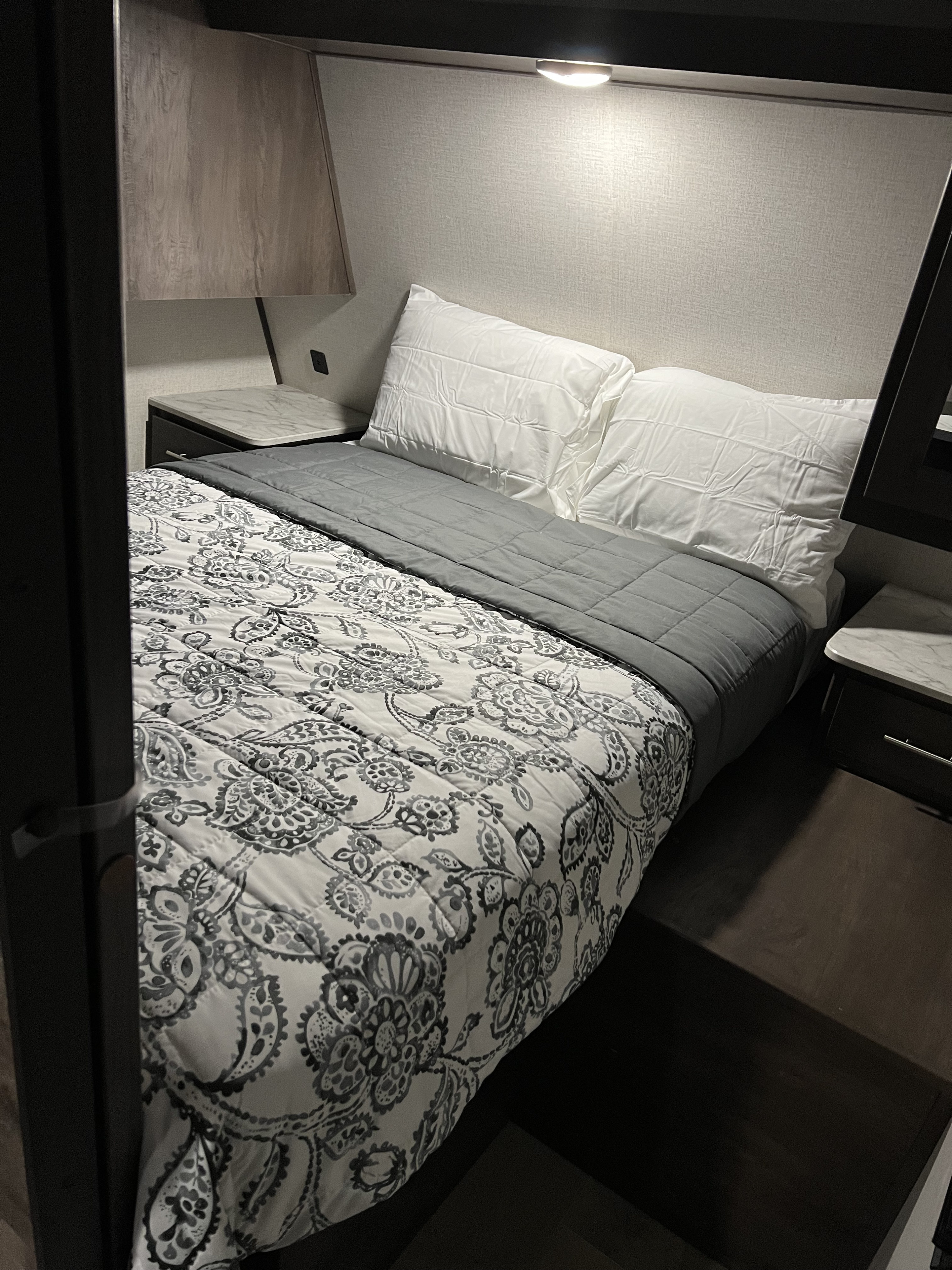 RV rental bedroom with a cozy bed, patterned comforter, white pillows, and practical nightstands with overhead lighting.. Dutchmen Coleman Lantern 2021