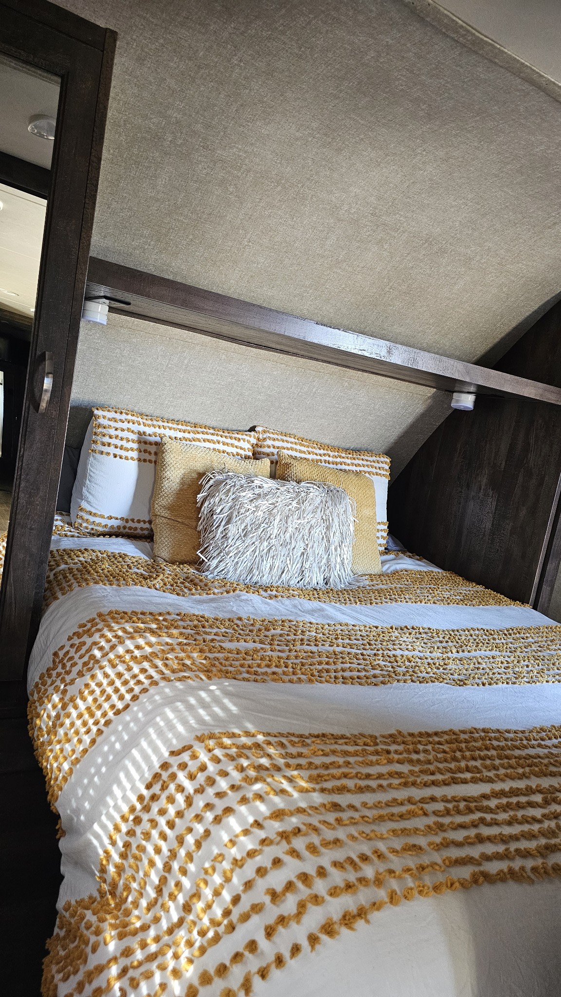 Bright RV rental bedroom: white bed with mustard yellow textured stripes, cozy pillows, and sunlight filtering in.. Forest River Vibe Extreme Lite 2017