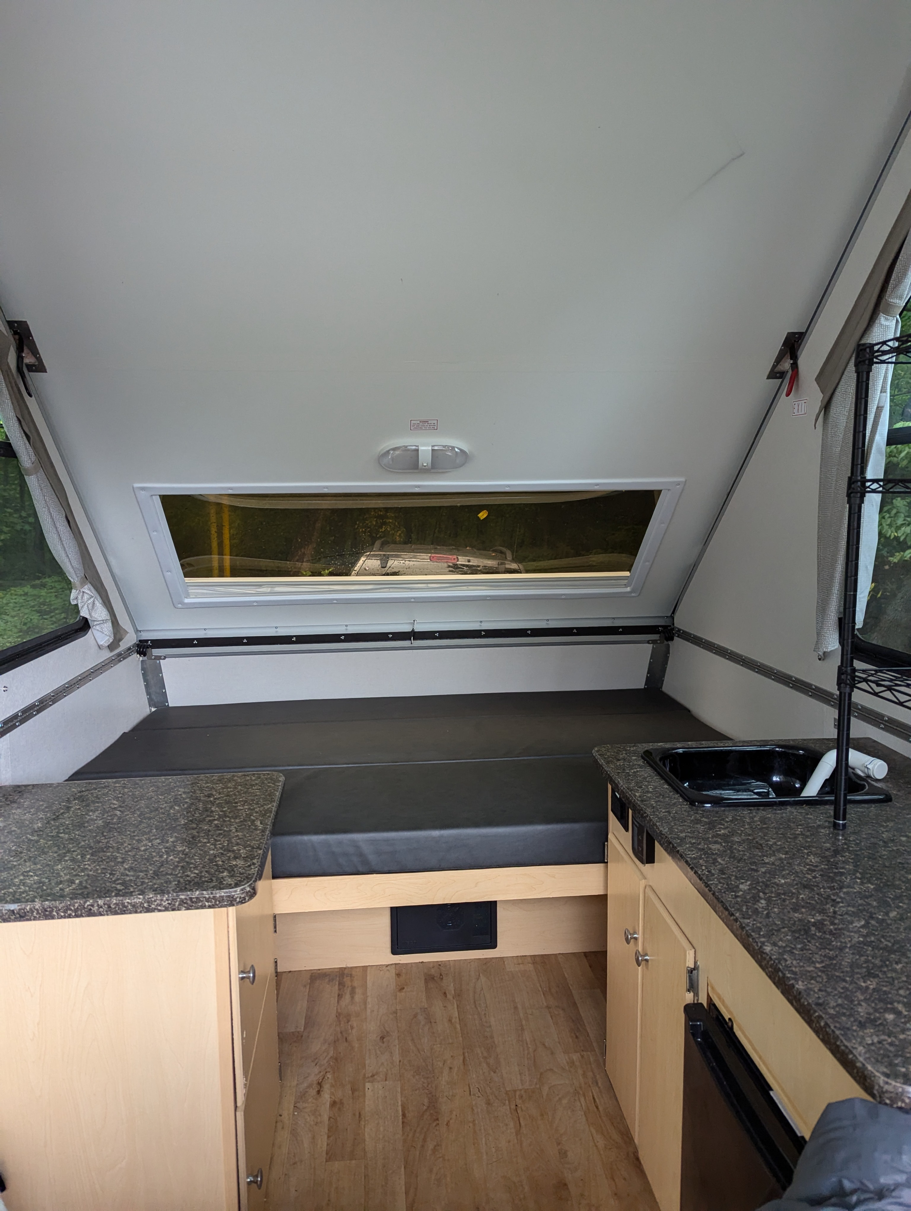 RV rental interior showing a bed, kitchen counter with sink, and wood storage cabinets. Bright, compact space.. A Liner A Liner Popup Trailer 2022