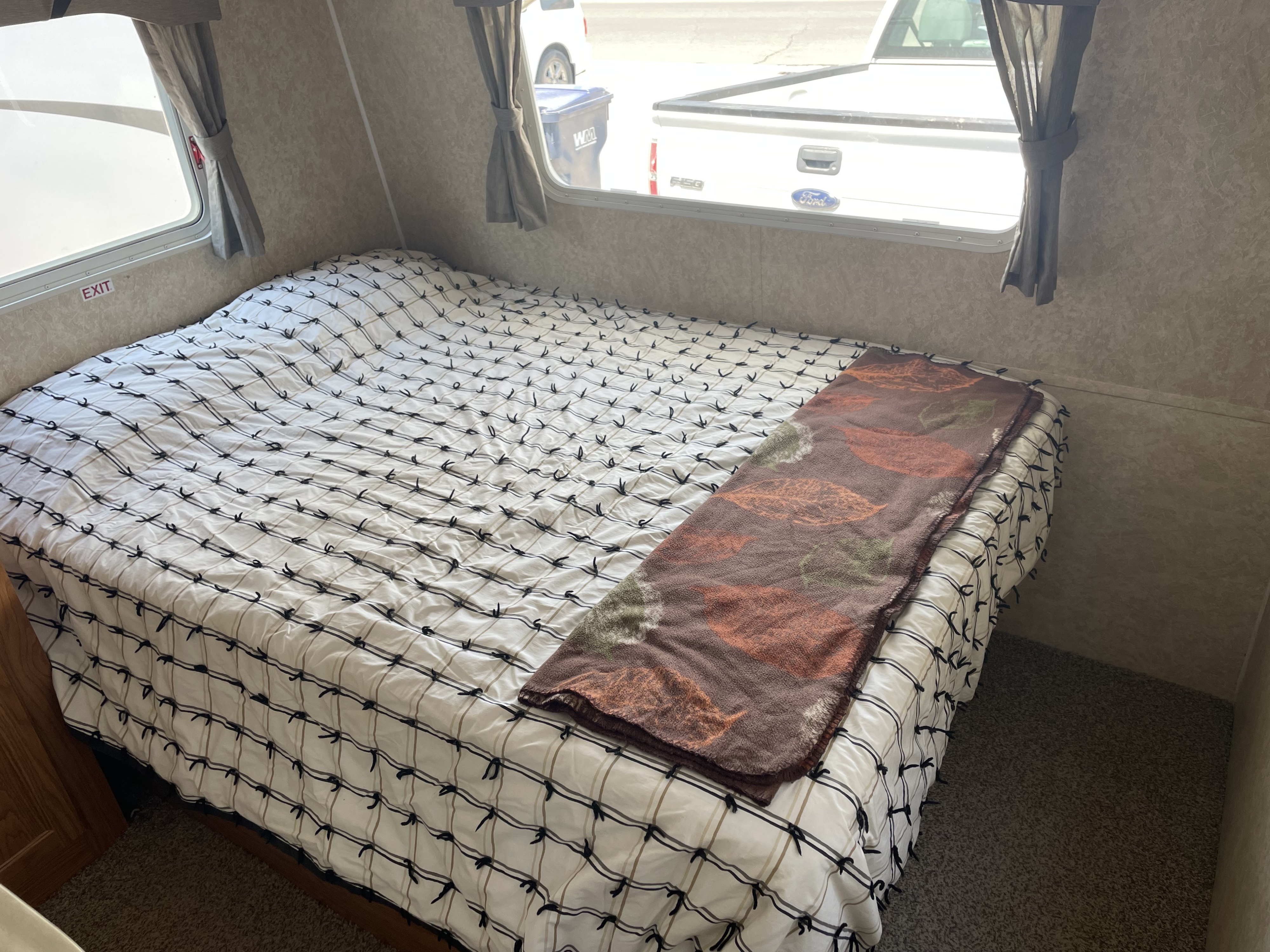 RV rental bedroom: bed with patterned comforter, leaf blanket, and windows showing an outside truck view.. Extreme RVs Sportsmaster 2007
