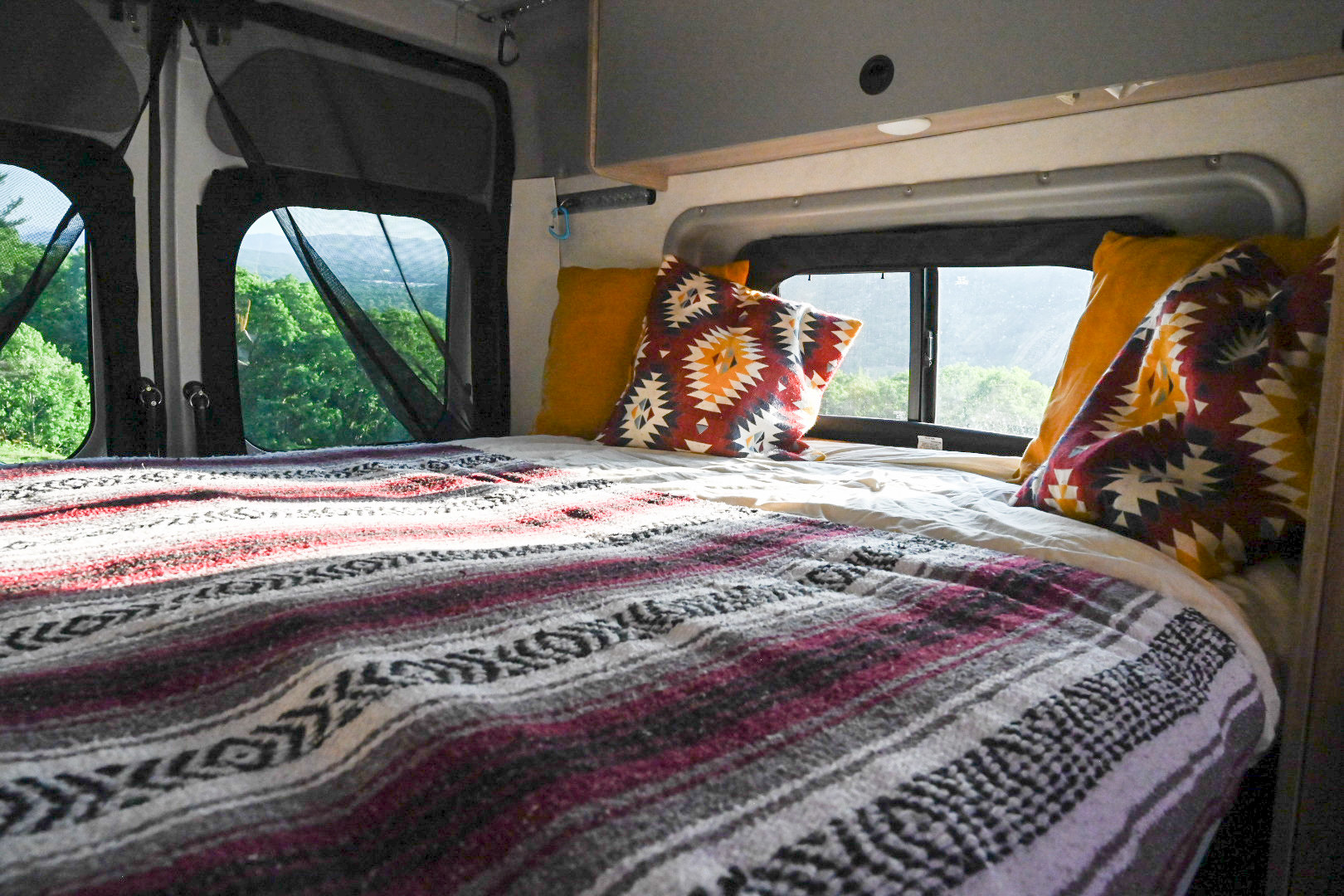 Cozy RV rental interior with bed, tribal blanket, and scenic forest views through netted windows.. Winnebago Solis 59PX 2021