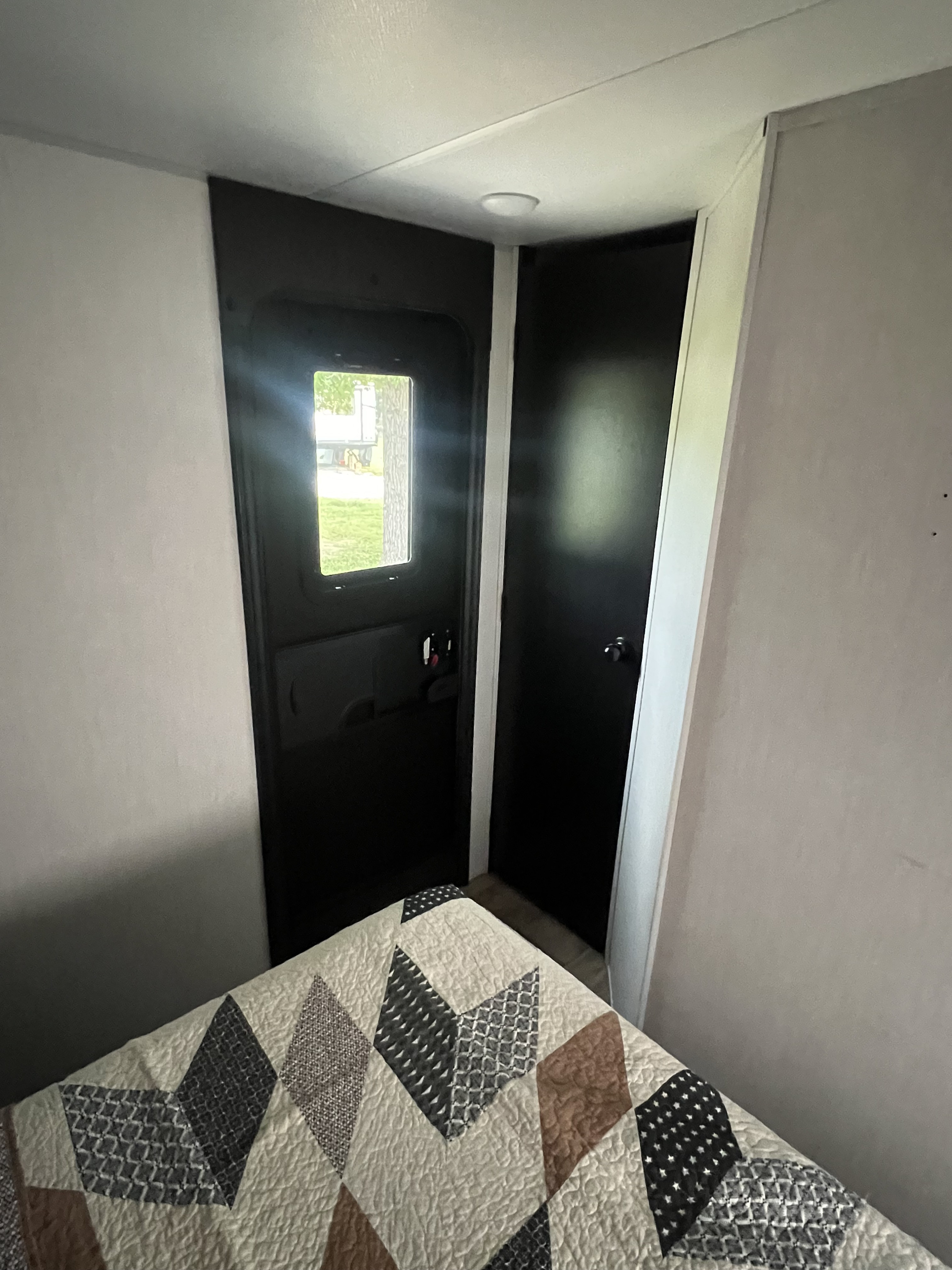 Cozy rv rental interior with patterned bed, main entry door with window, and a second interior door.. Forest River Cherokee Grey Wolf 2022