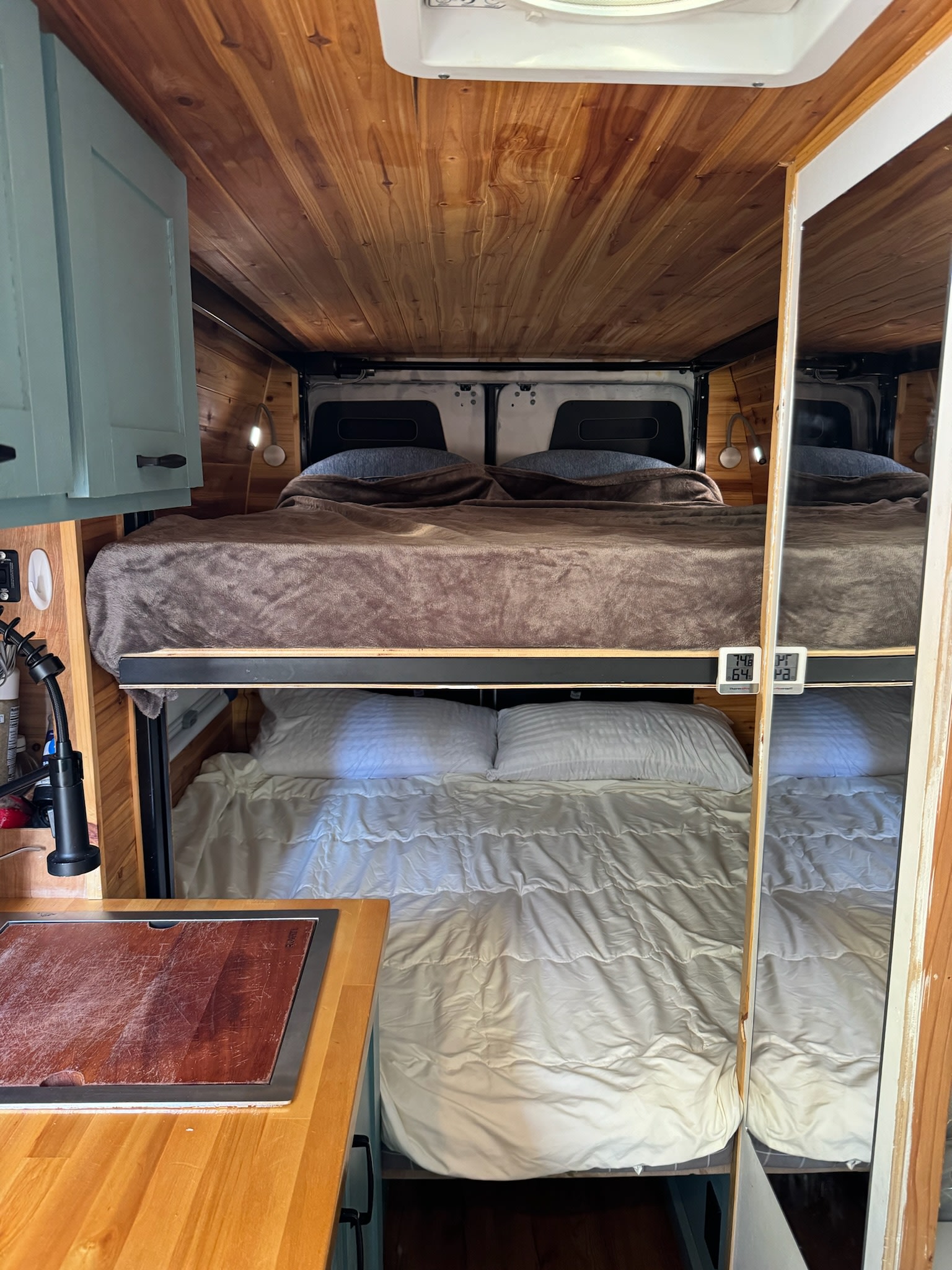 Inside a cozy RV rental: two bunk beds with soft bedding, warm wood accents, and a compact kitchen area.. Mercedes-Benz Sprinter 2021