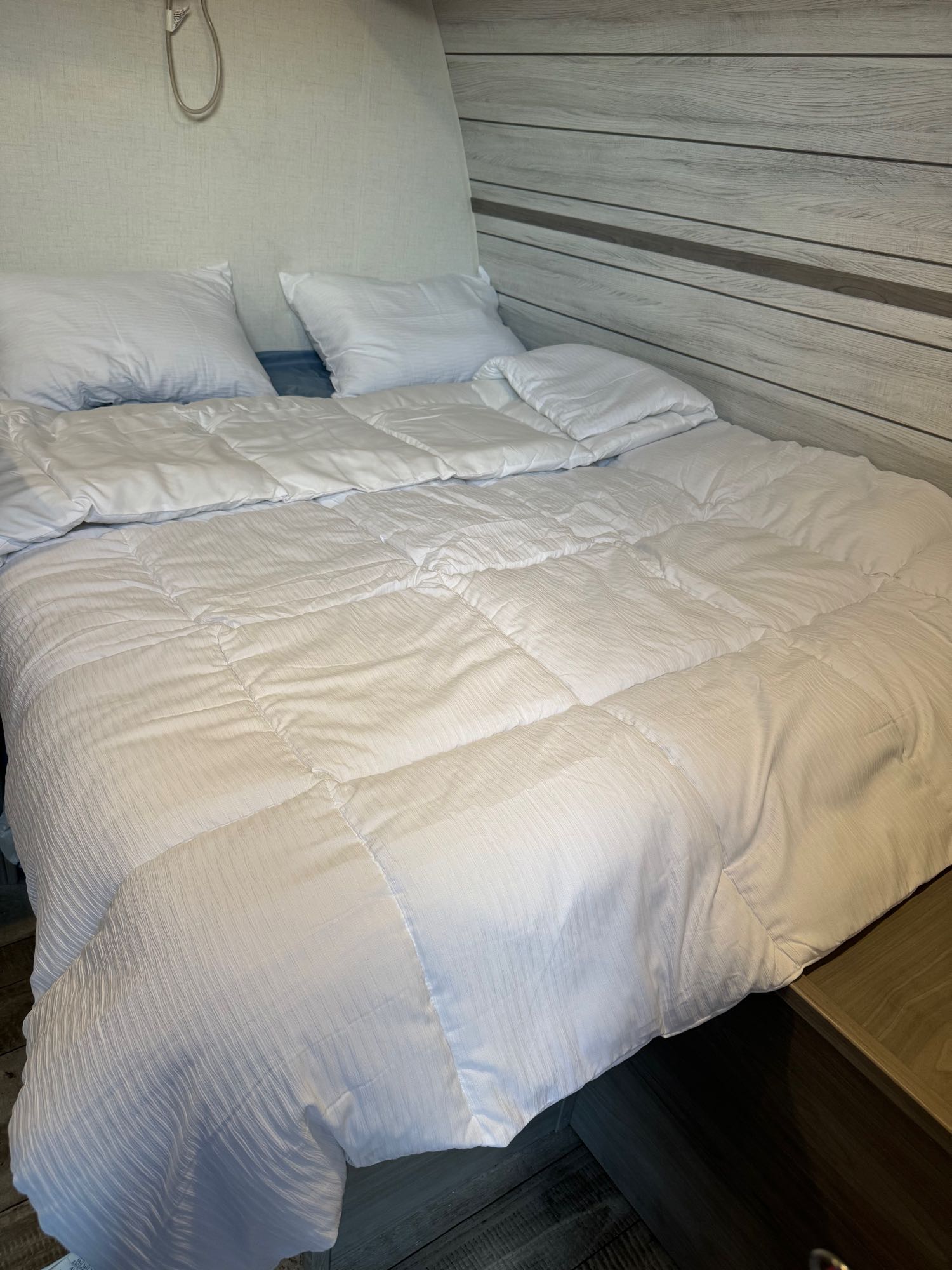 Cozy bed in an RV rental, with white bedding & wooden wall accents, perfect for a comfortable night.. Dutchmen Coleman 17B 2024