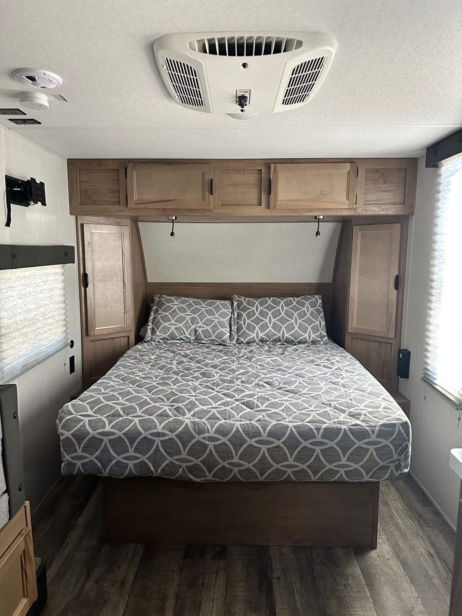 RV rental bedroom: a bed with patterned bedding, overhead storage, AC, and wood-look flooring.. Forest River Cherokee Wolf Pup Black Label 2024