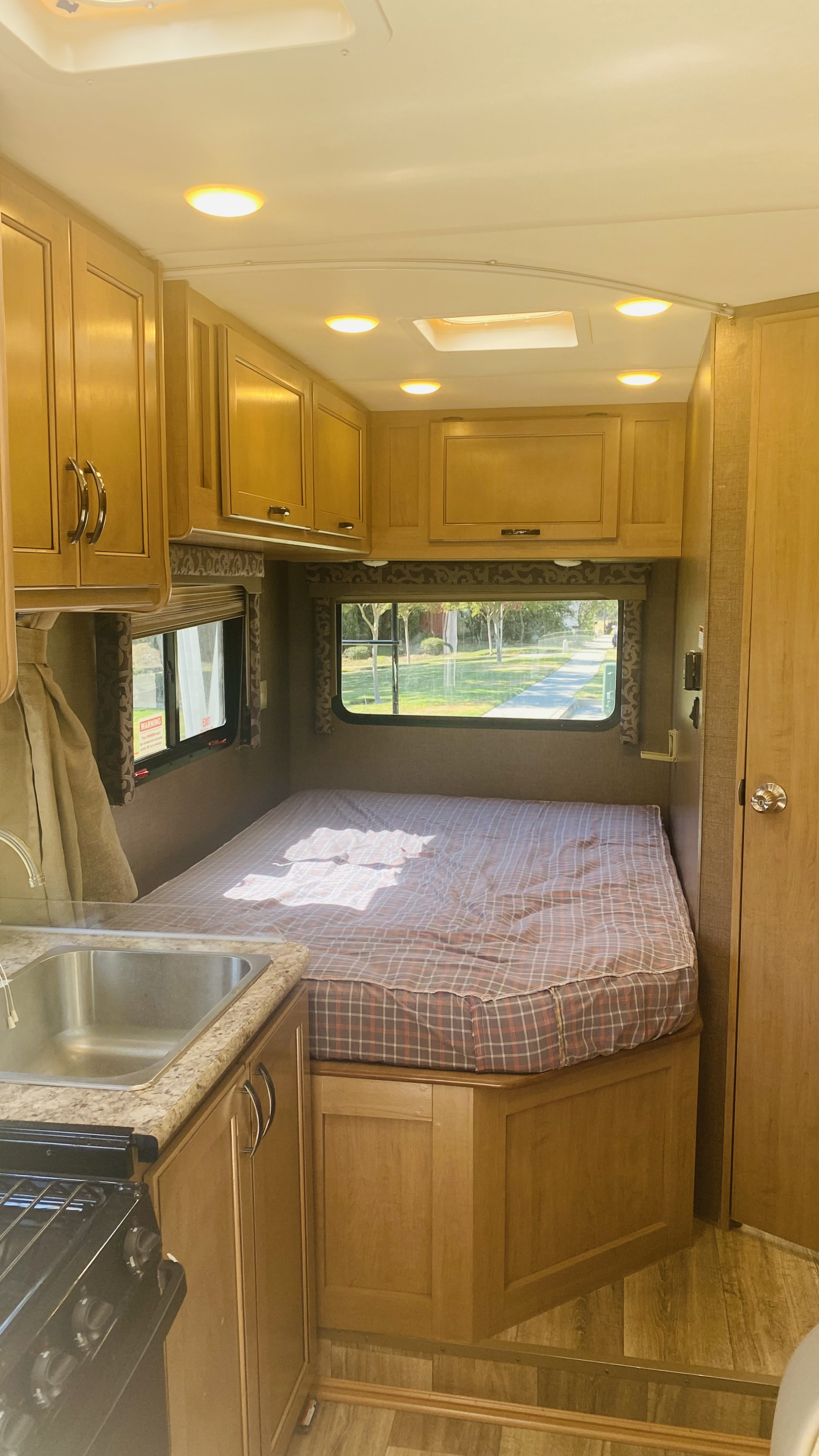 Explore this spacious RV rental interior! Features a rear bed, kitchen with sink & stove, and ample wood cabinets for a comfy travel experience.. Thor Four Winds 2019