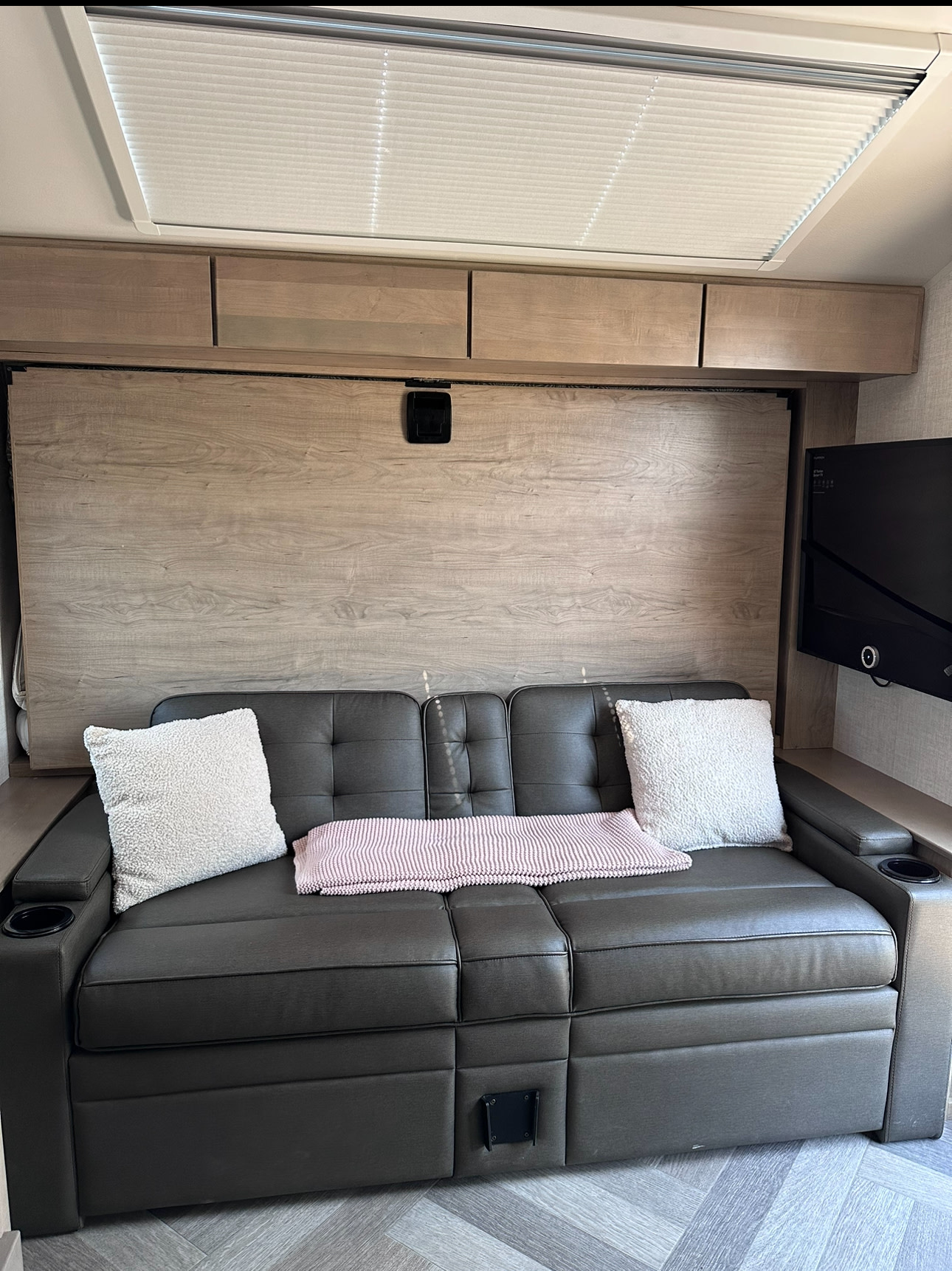 Inside this RV rental: a comfy dark sofa with pillows and blanket, smart overhead storage, and a mounted TV. Note the murphy bed wall.. Ember Overland 2023