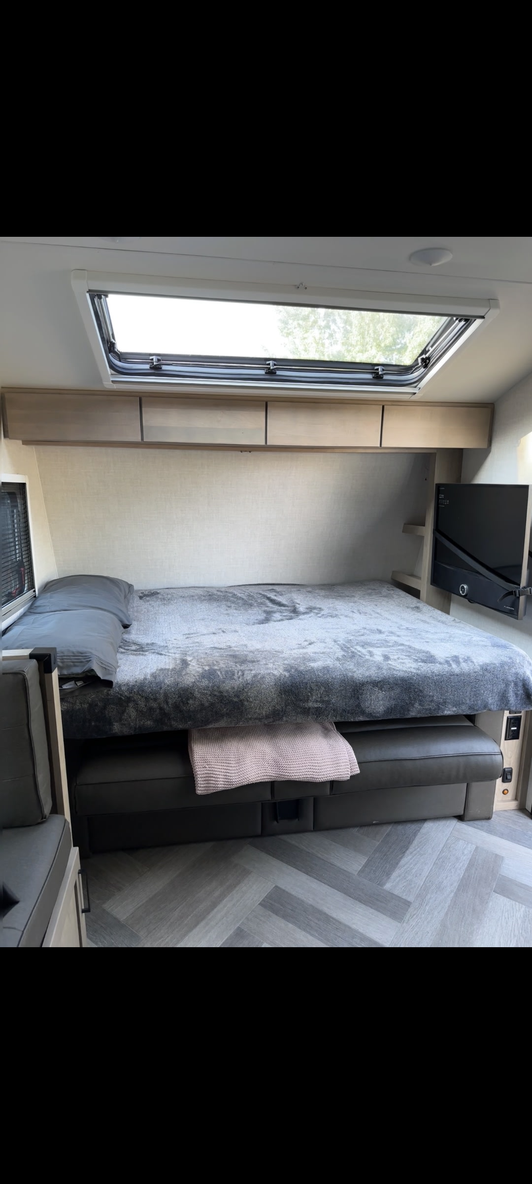 Cozy RV rental bedroom with comfy bed, skylight, overhead storage, and TV. Herringbone floor accents this travel trailer.. Ember Overland 2023