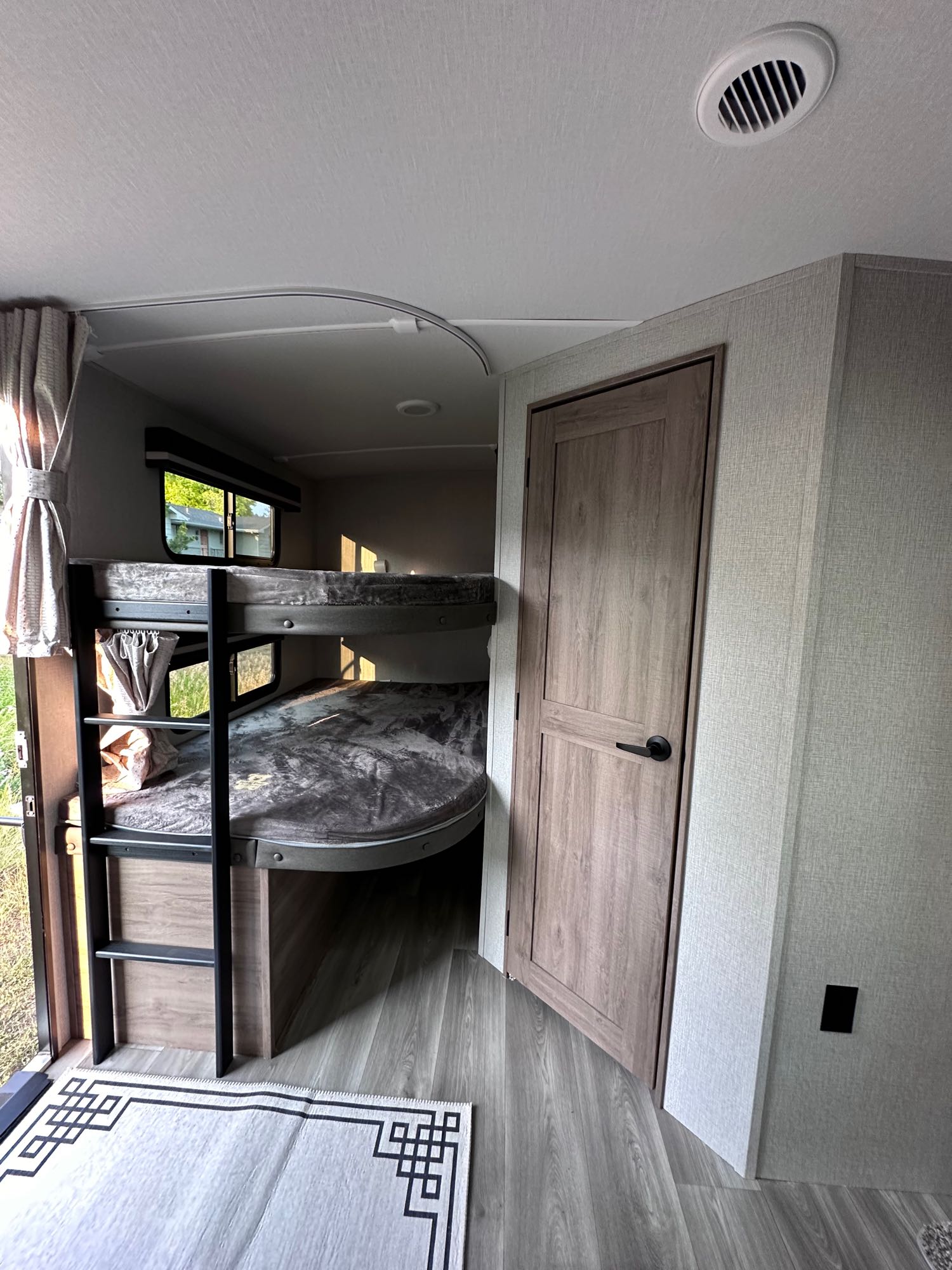 Inside an RV rental: modern bunk beds with ladder, a wood-paneled door, and bright, clean living space.. Grand Design Imagine 2024