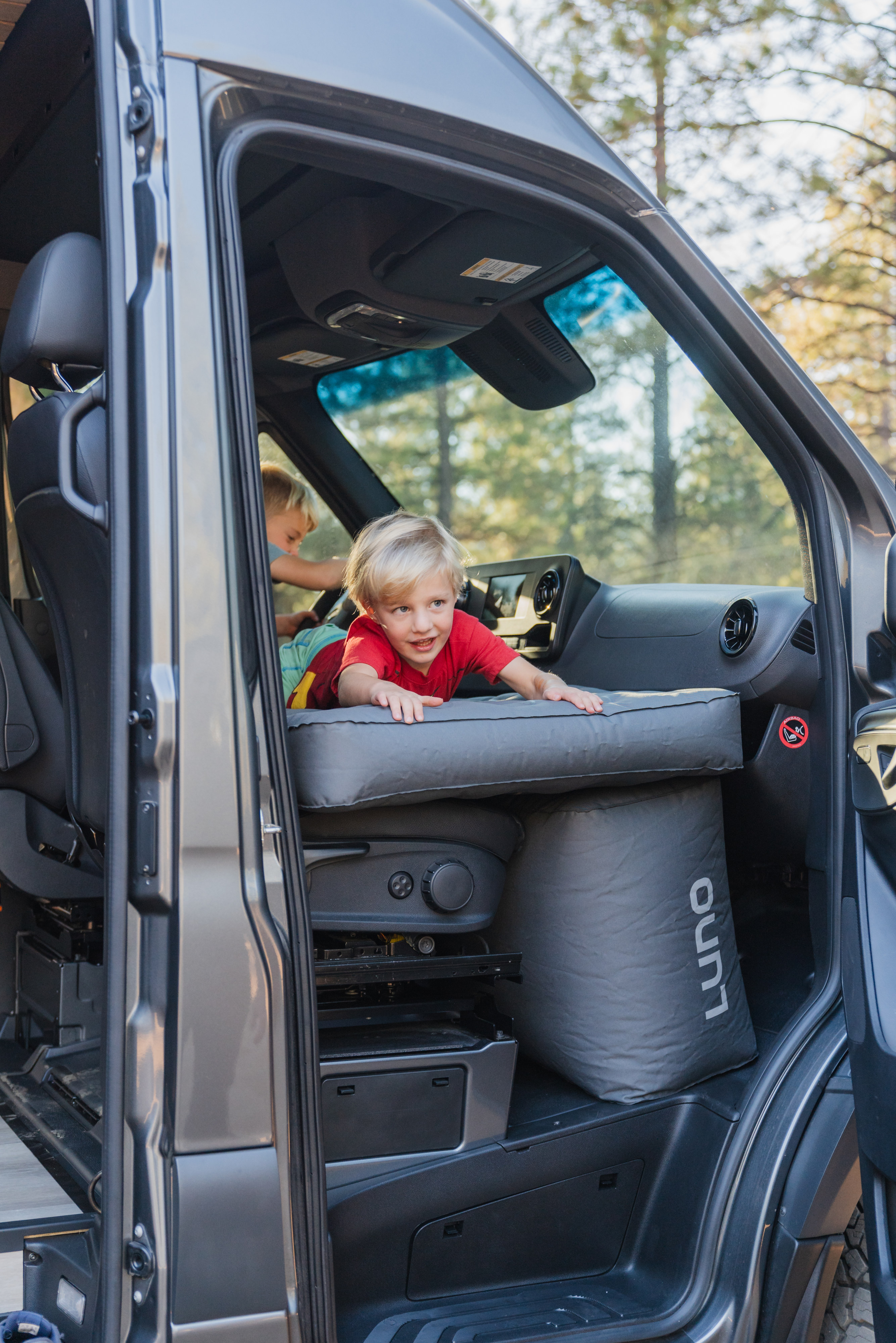 Two young boys play in an RV rental van. An inflatable pad fills the footwell, creating extra space for family travel.. Ford Transit 350 2019