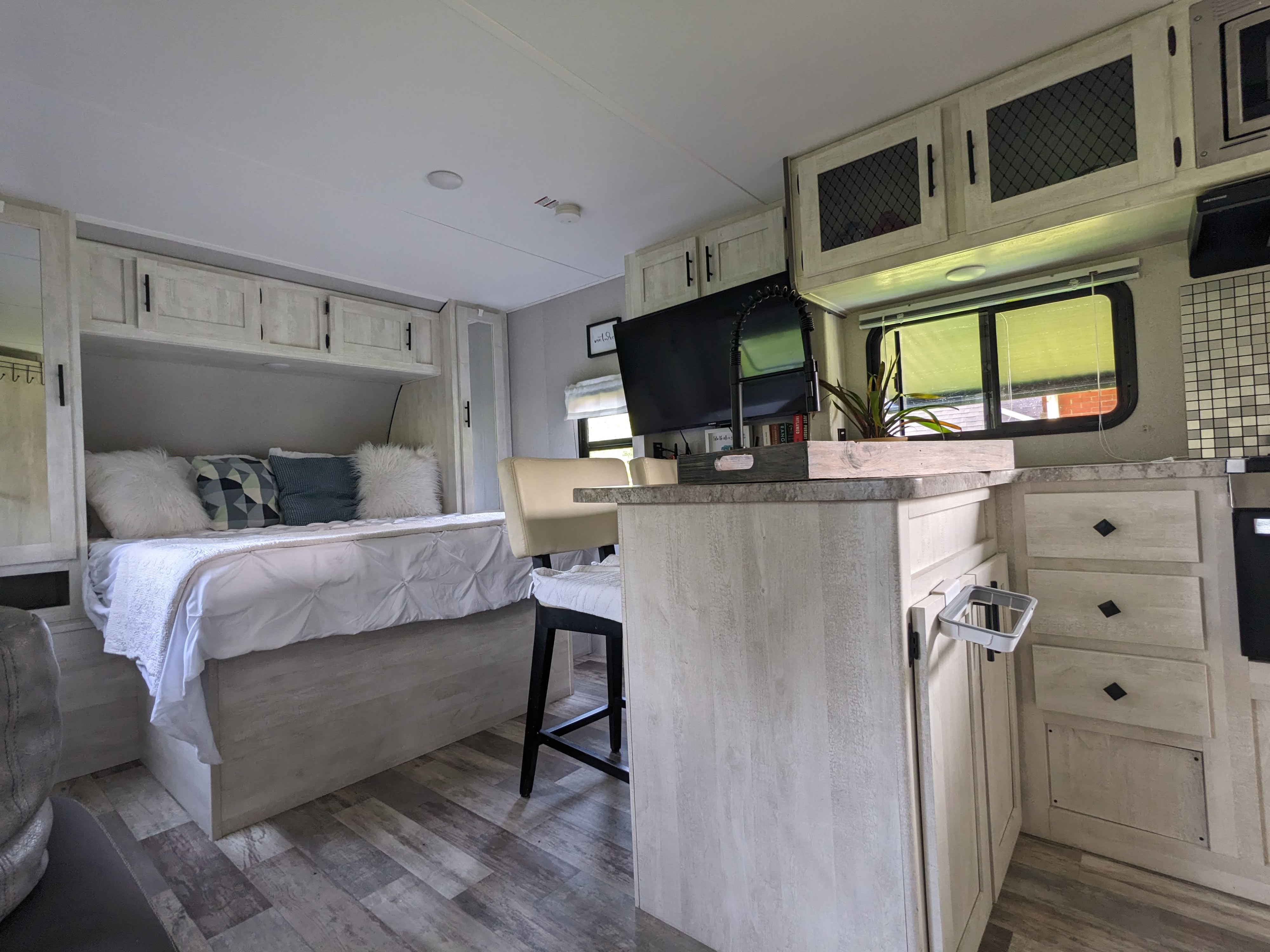 Cozy RV rental interior showing a compact bedroom with a bed and overhead cabinets, alongside a functional kitchen/living area.. Forest River Shasta 2020