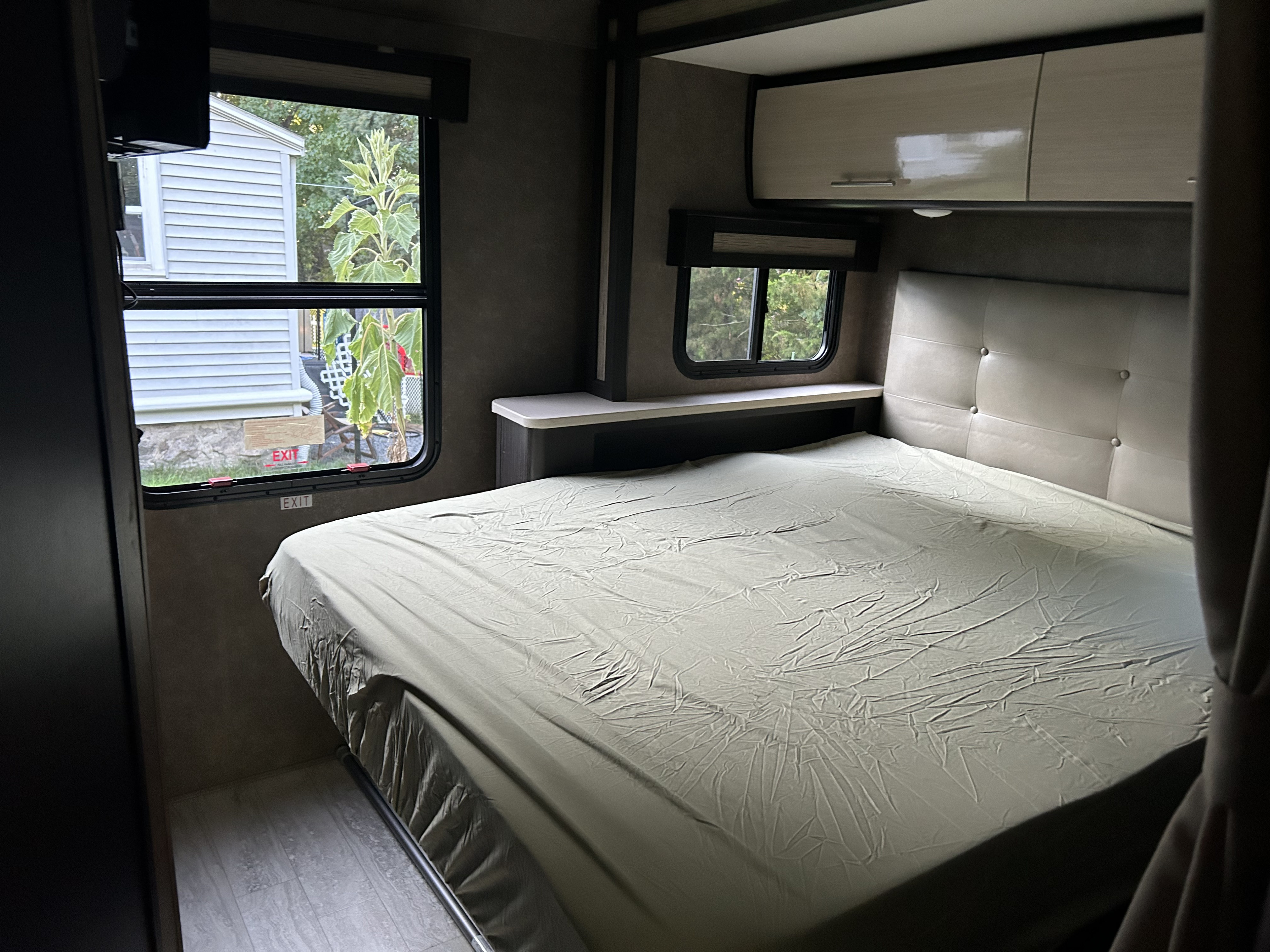 Inside this RV rental's bedroom: a spacious bed with a light-colored sheet, padded headboard, and windows revealing outdoor scenery.. Thor Gemini 2017